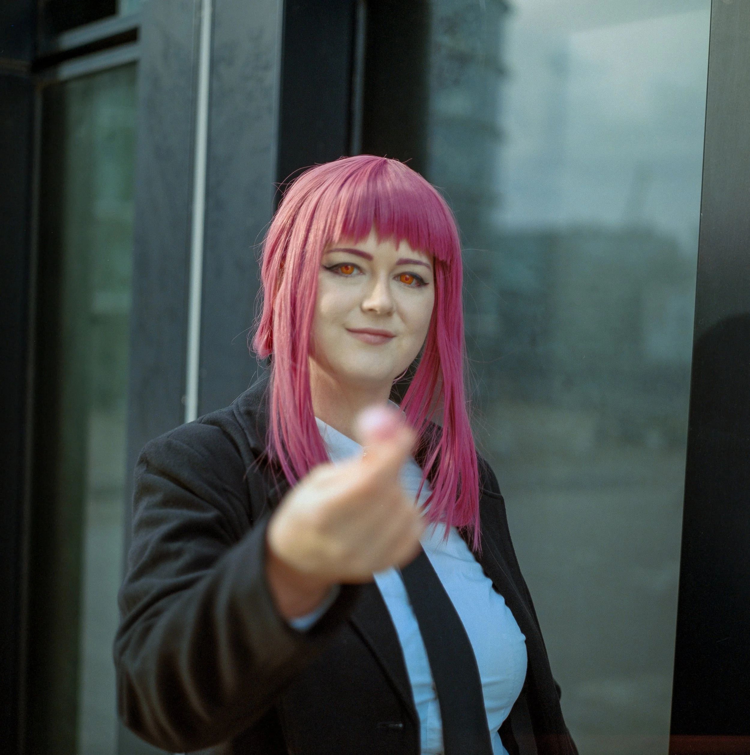 Frau mit pinkem Haar und orangefarbenen Augen zeigt mit dem Finger in die Kamera.