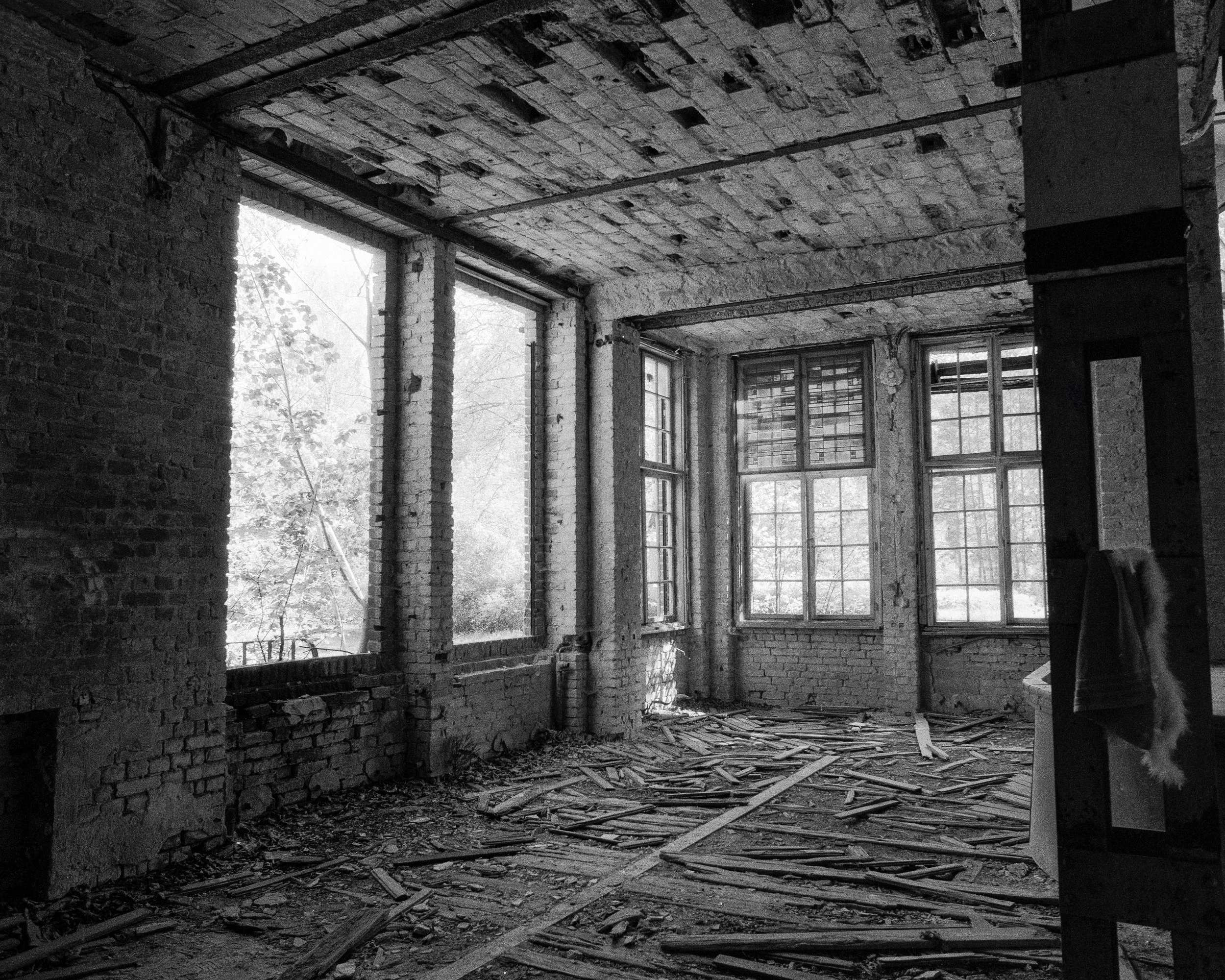 Verlassener, leerer Raum mit großen Fenstern, zerbrochenen Fensterscheiben und heruntergefallenem Holz auf dem Boden, Wände und Decke aus alten Ziegeln.