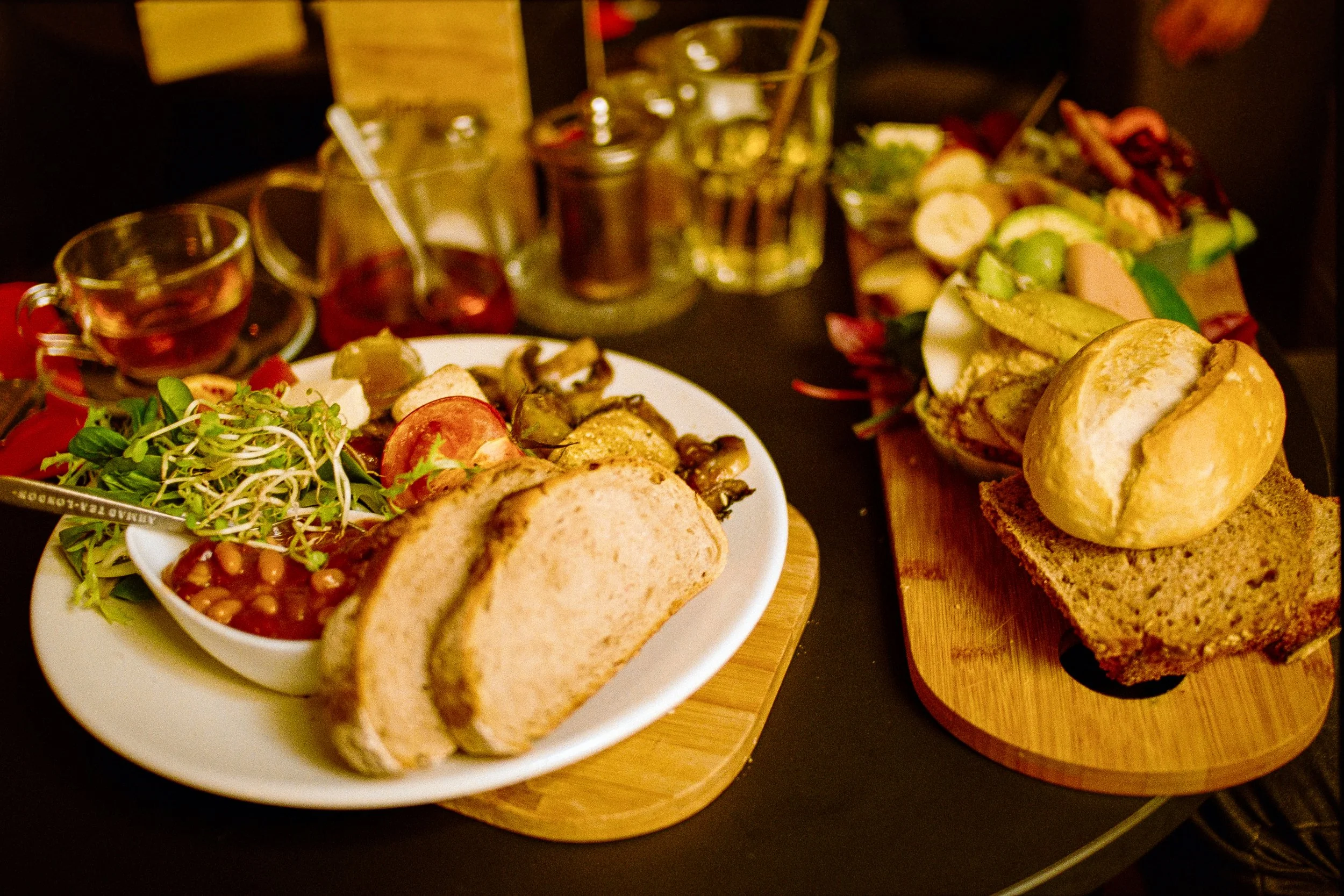 Ein gedeckter Tisch mit Sandwiches, Salat, Sprossen, Tomaten, Gurken, verschiedenen Aufschnittsorten, Bier und Weingläser.
