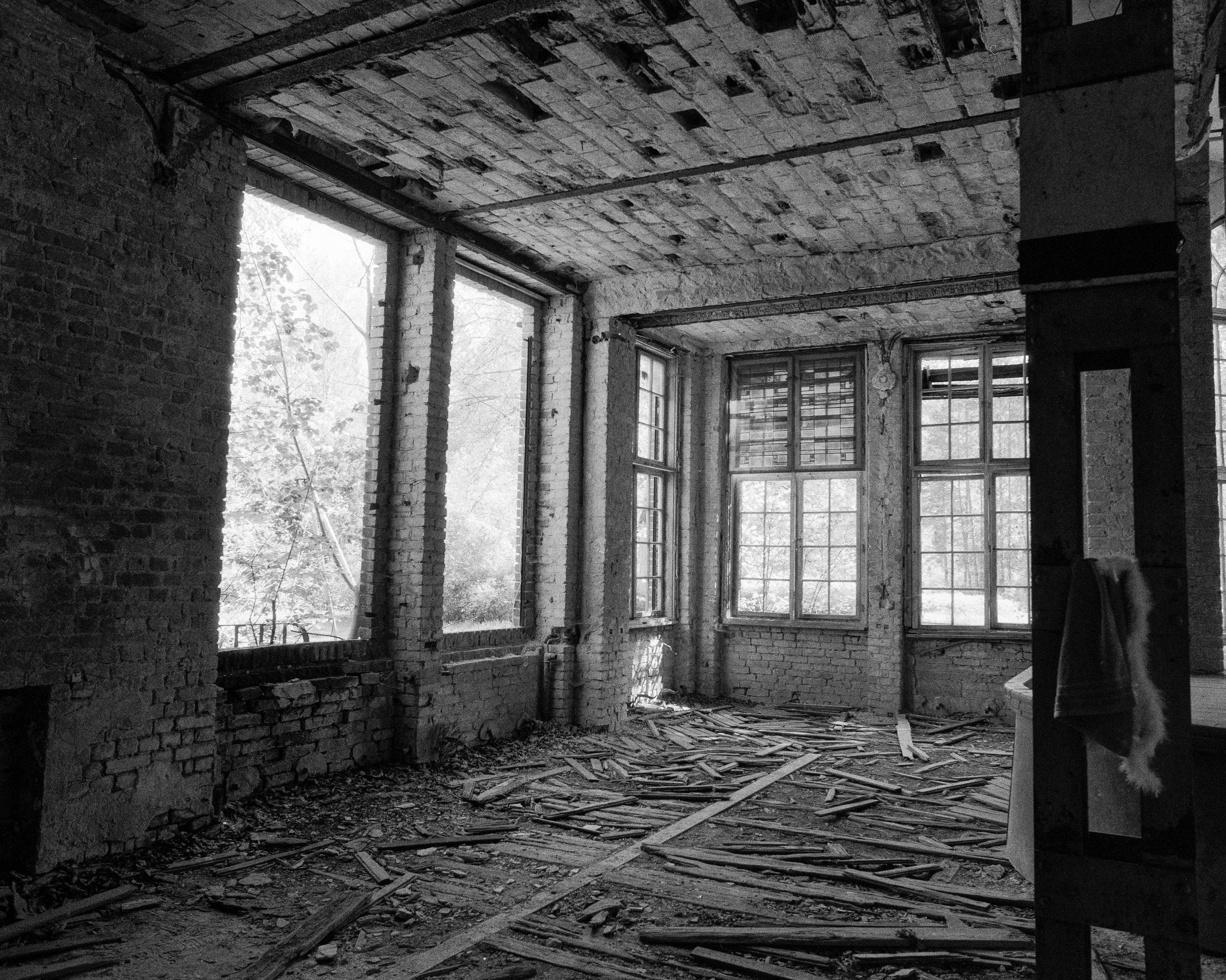 Innenaufnahme eines verfallenen Gebäudes mit bröckelnden Wänden, Holztreppen, zerbrochenen Fenstern und auf dem Boden verstreutem Holz.