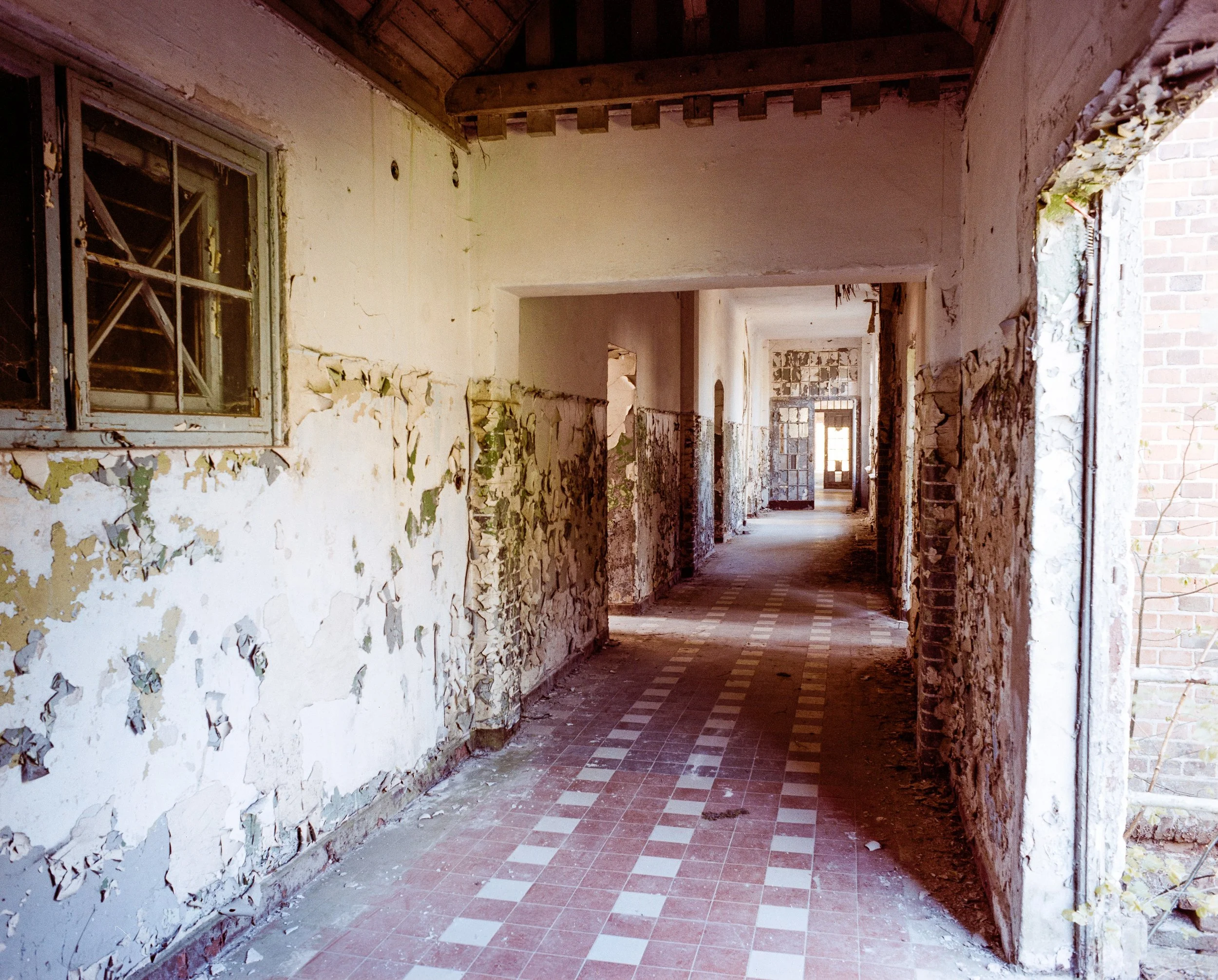 Verlassener Flur in einem alten Gebäude mit abblätternder Wandfarbe und kaputten Fenstern.