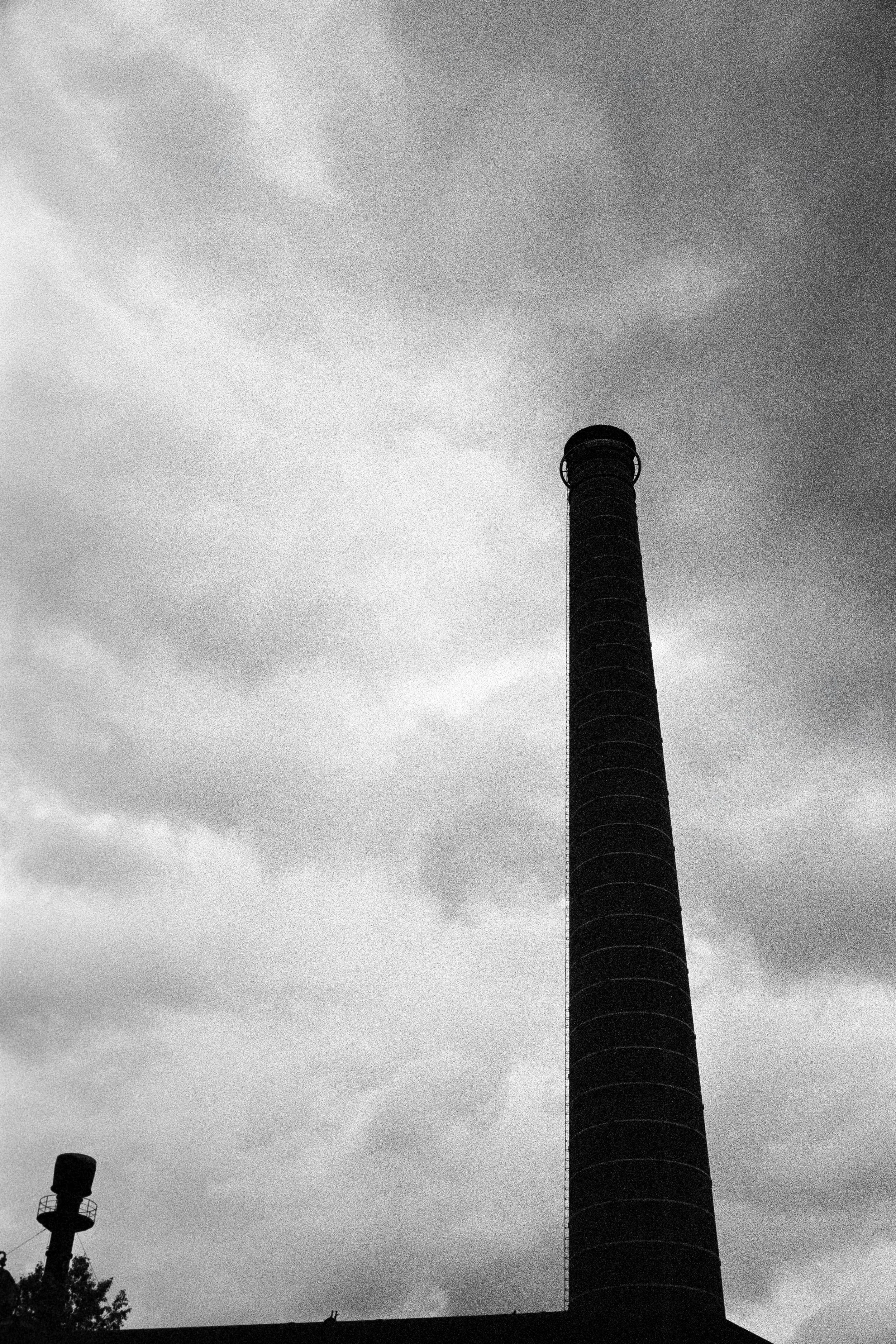 Schwarz-weiß-Bild eines hohen Industrie-Schornsteins gegen einen bewölkten Himmel.