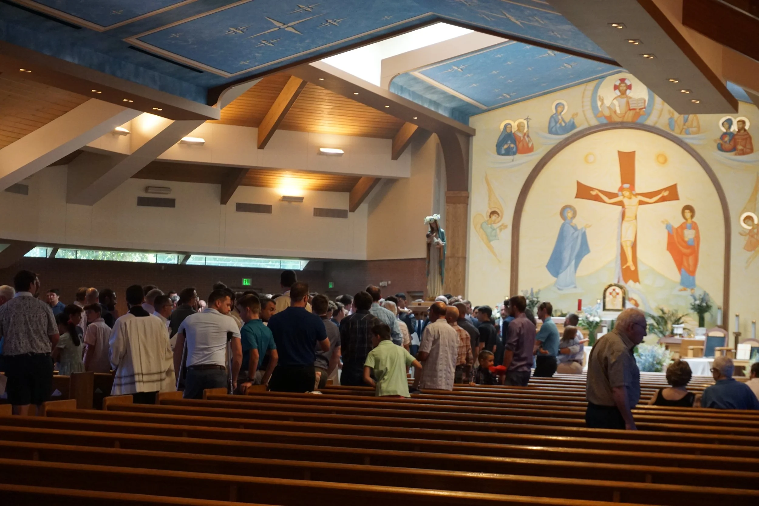 People gathered inside a church near the altar with religious statues and paintings, including a large mural of Jesus on the cross.