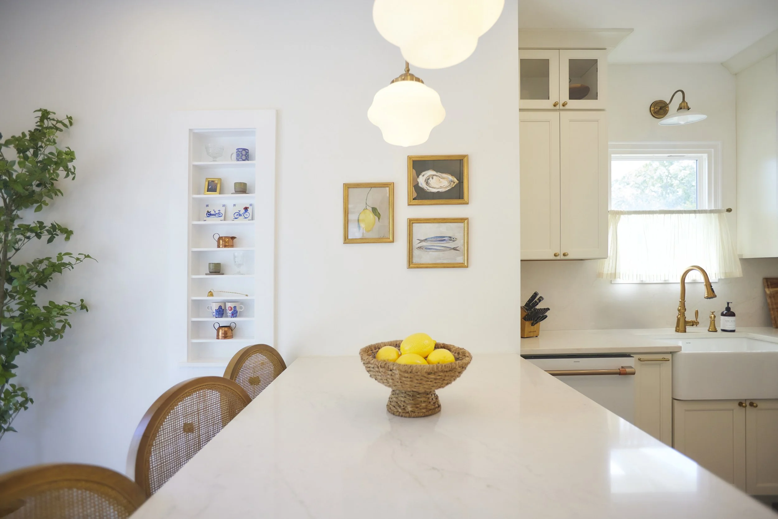 Bright kitchen with white cabinets, a white marble countertop, a basket of lemons, and wall art of fruits and fish.