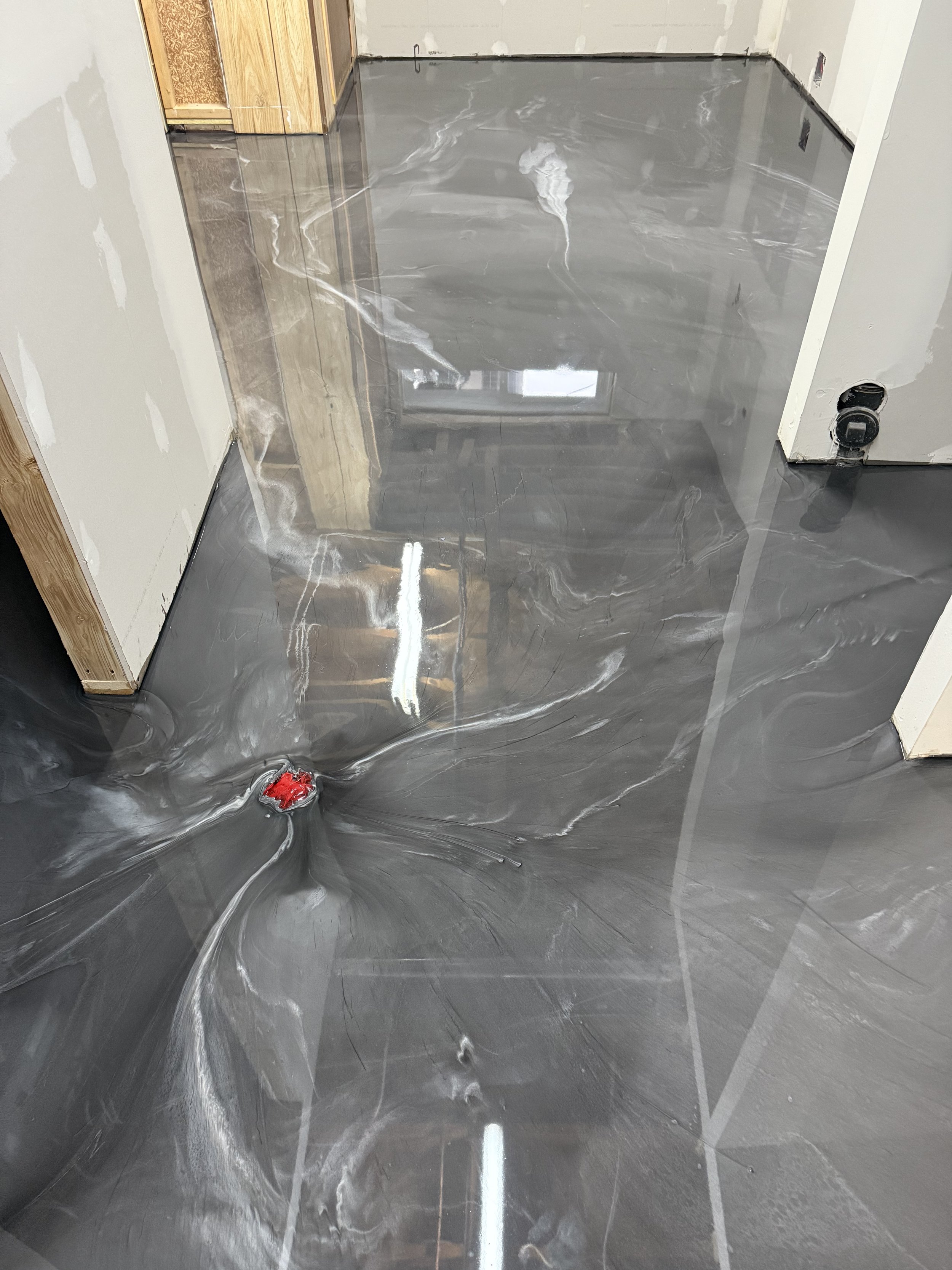 Marble epoxy finish with medium grey with white veins, and reflective surface in an unfinished room with exposed drywall and wooden framing.