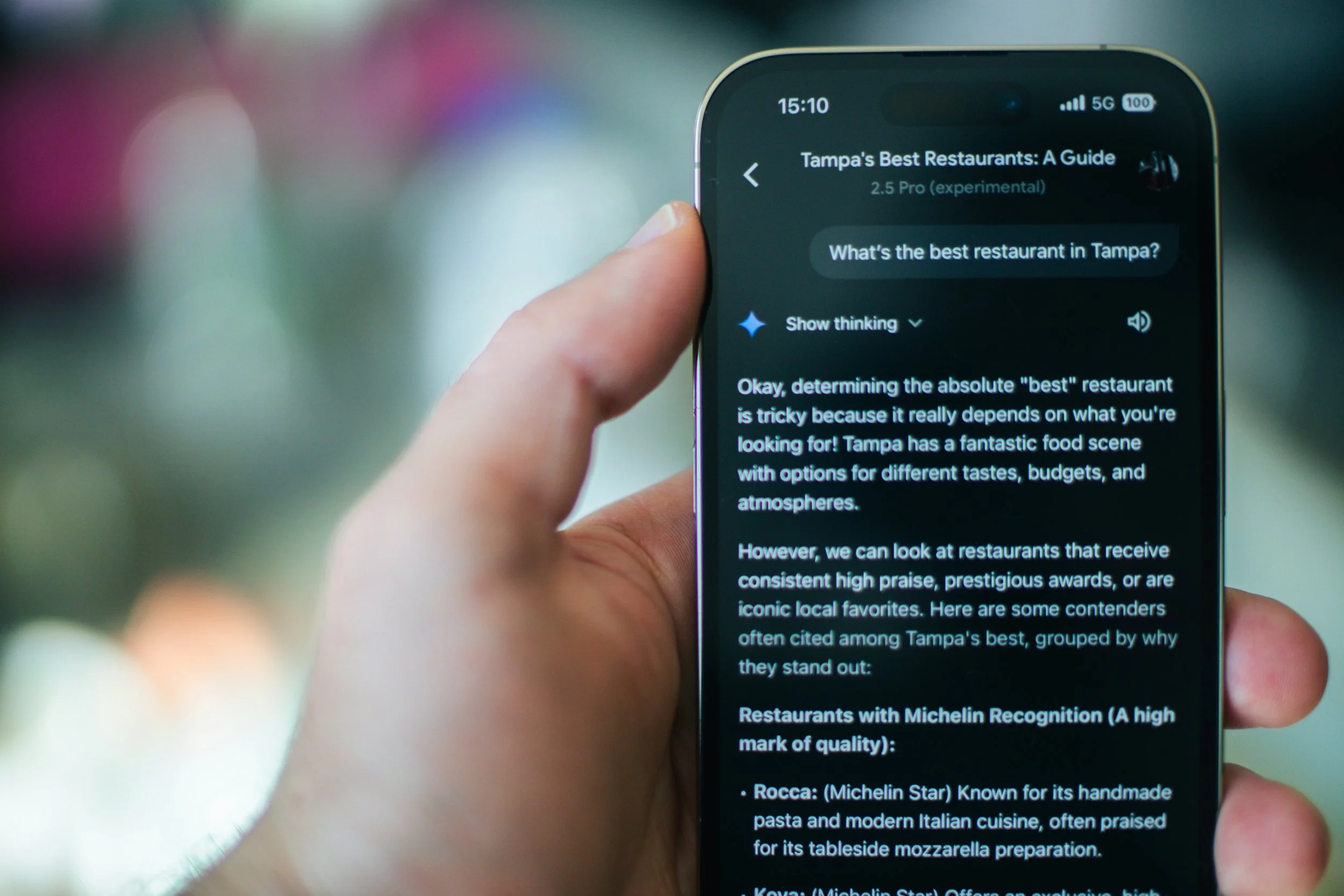 Close-up of a person's hand holding a smartphone displaying a guide about Tampa's best restaurants with text on the screen.