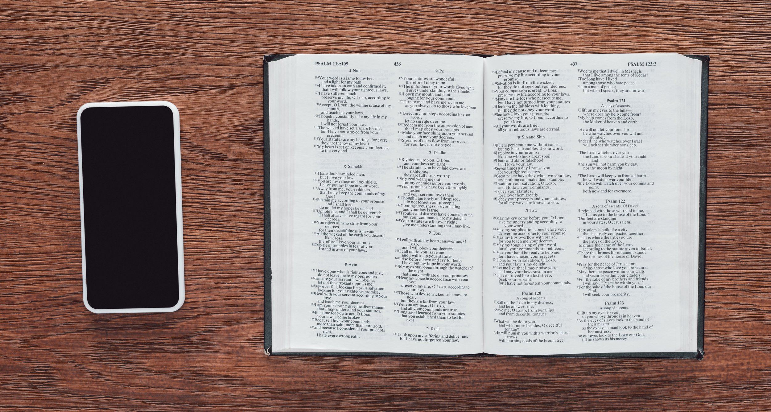 Open Bible beside a smartphone on a wooden table