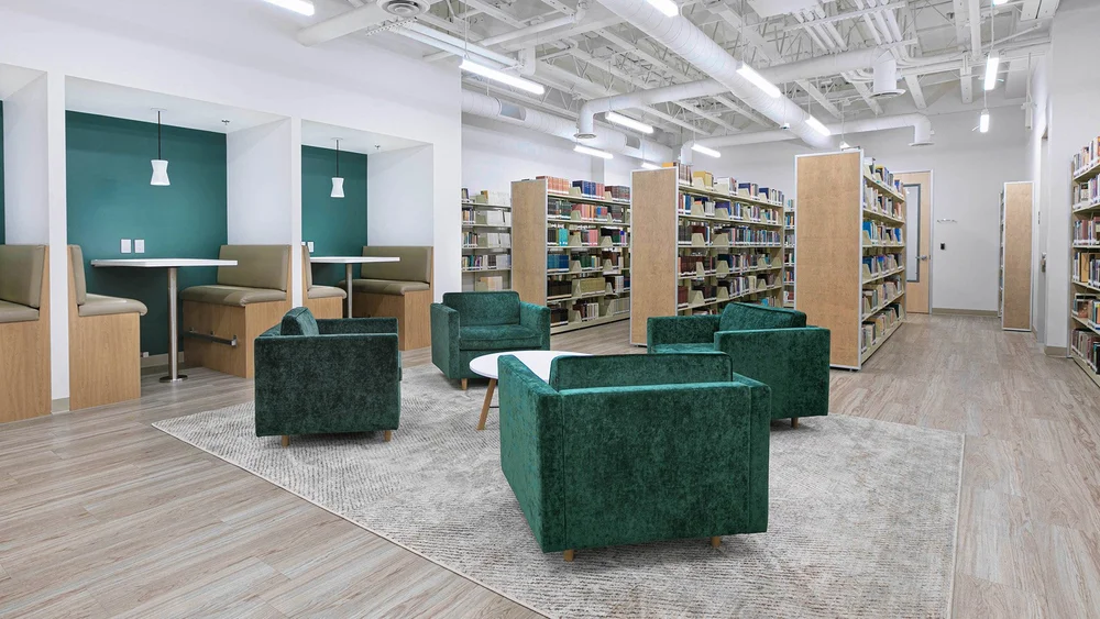 Green velvet armchairs around a coffee table beside bookshelves and a booth study nook in the CBI Lounge