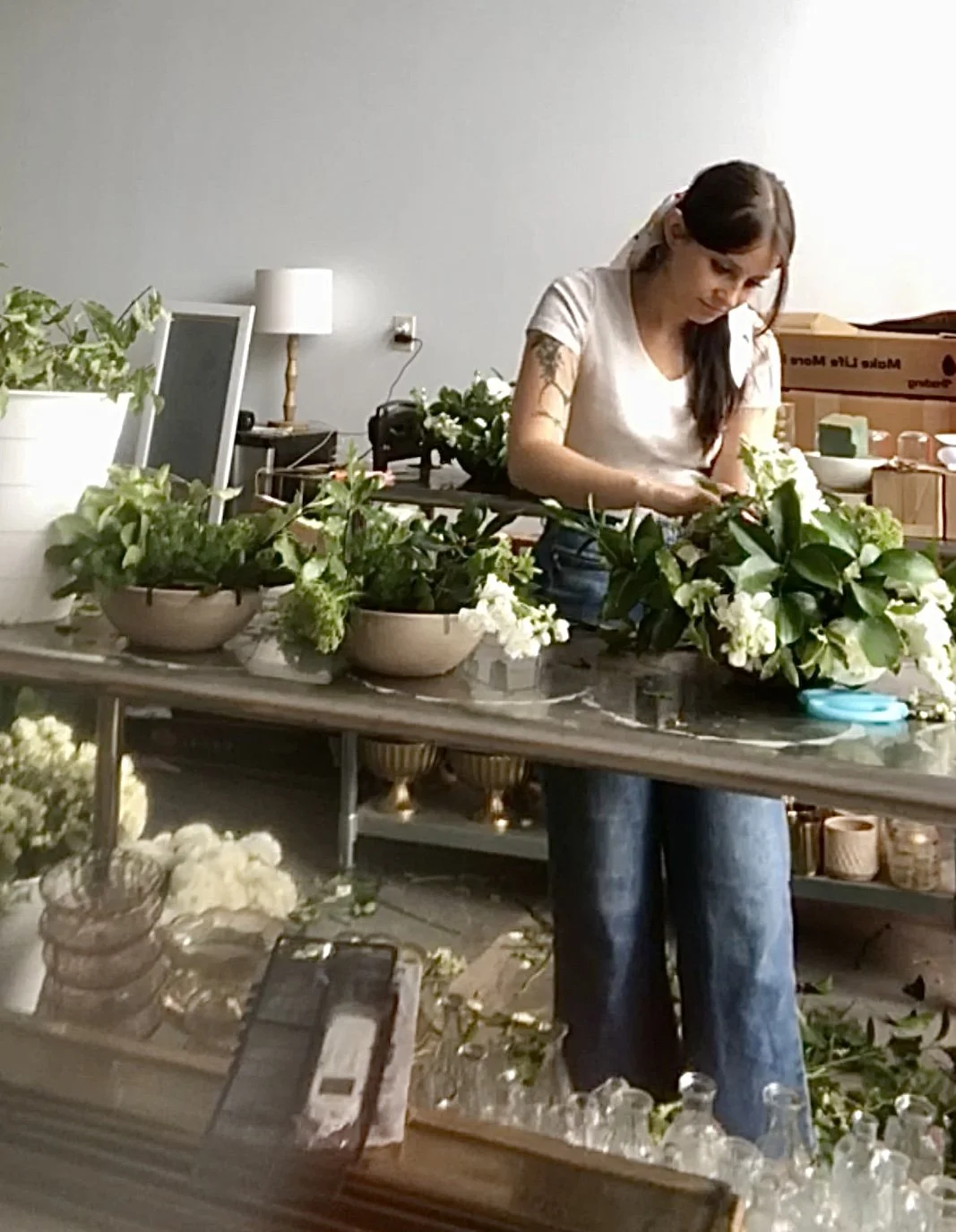 woman arranging white flowers and greenery on a table in a room
