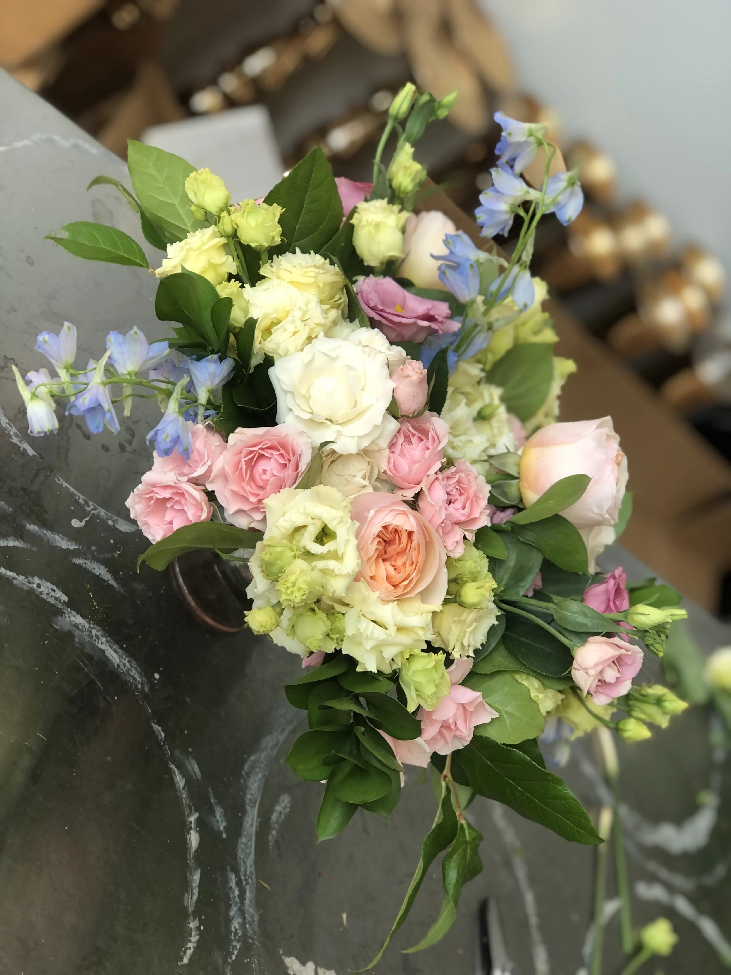 A bouquet of pink, white, and yellow flowers with green leaves, placed on a glass surface.