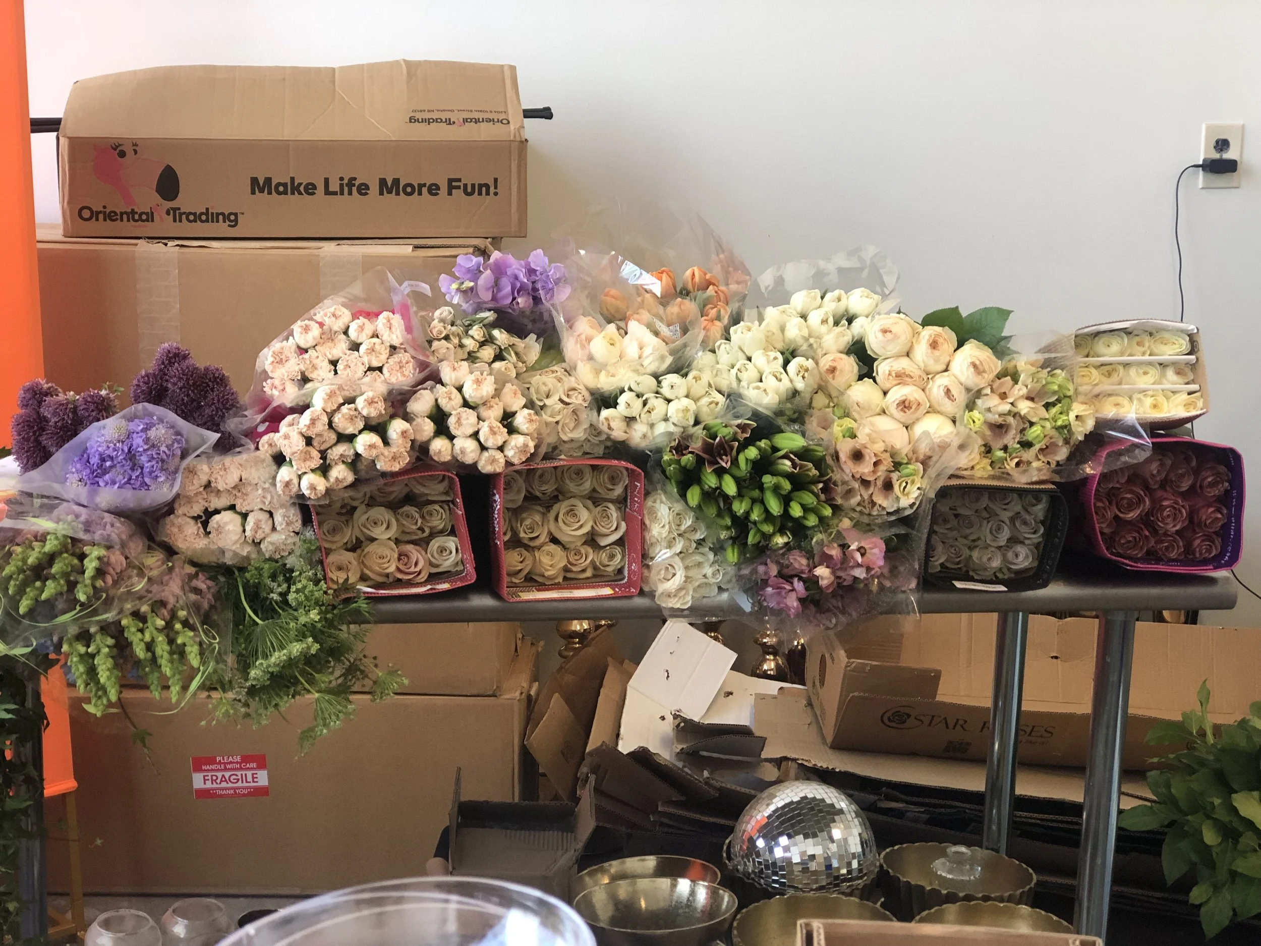 Various bouquets of flowers, primarily roses and other floral arrangements, placed on a metal table with cardboard boxes and miscellaneous items in the background.