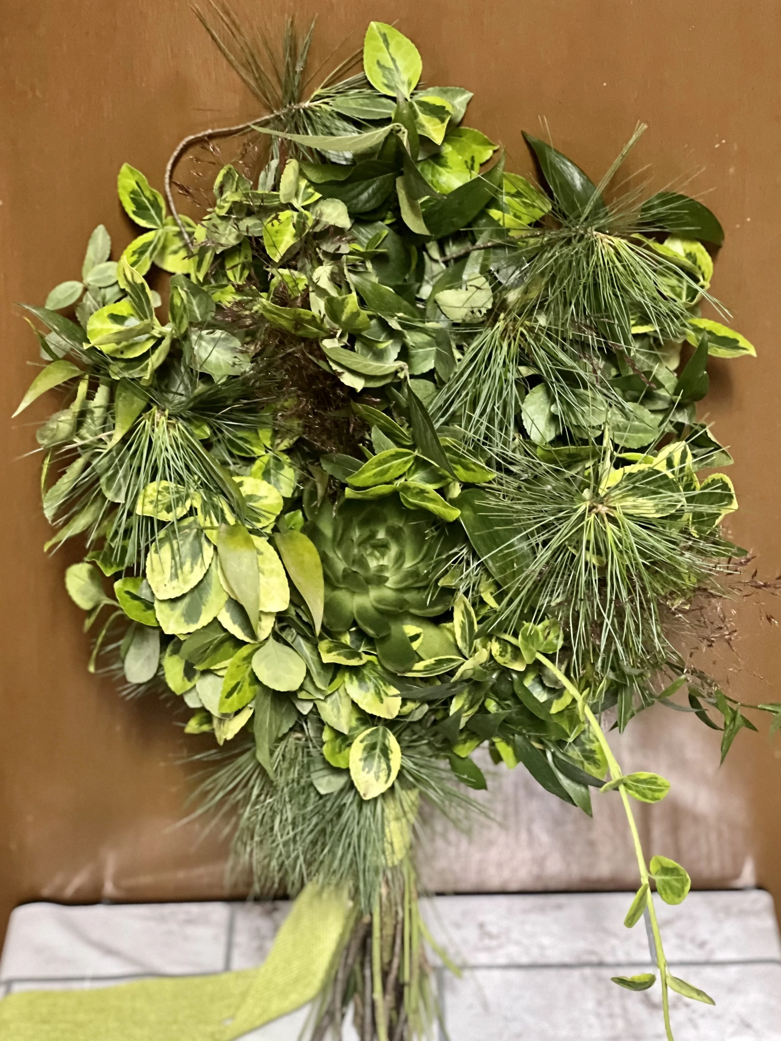 A bouquet of various green leaves and plants on a brown surface with a white tiled area underneath.