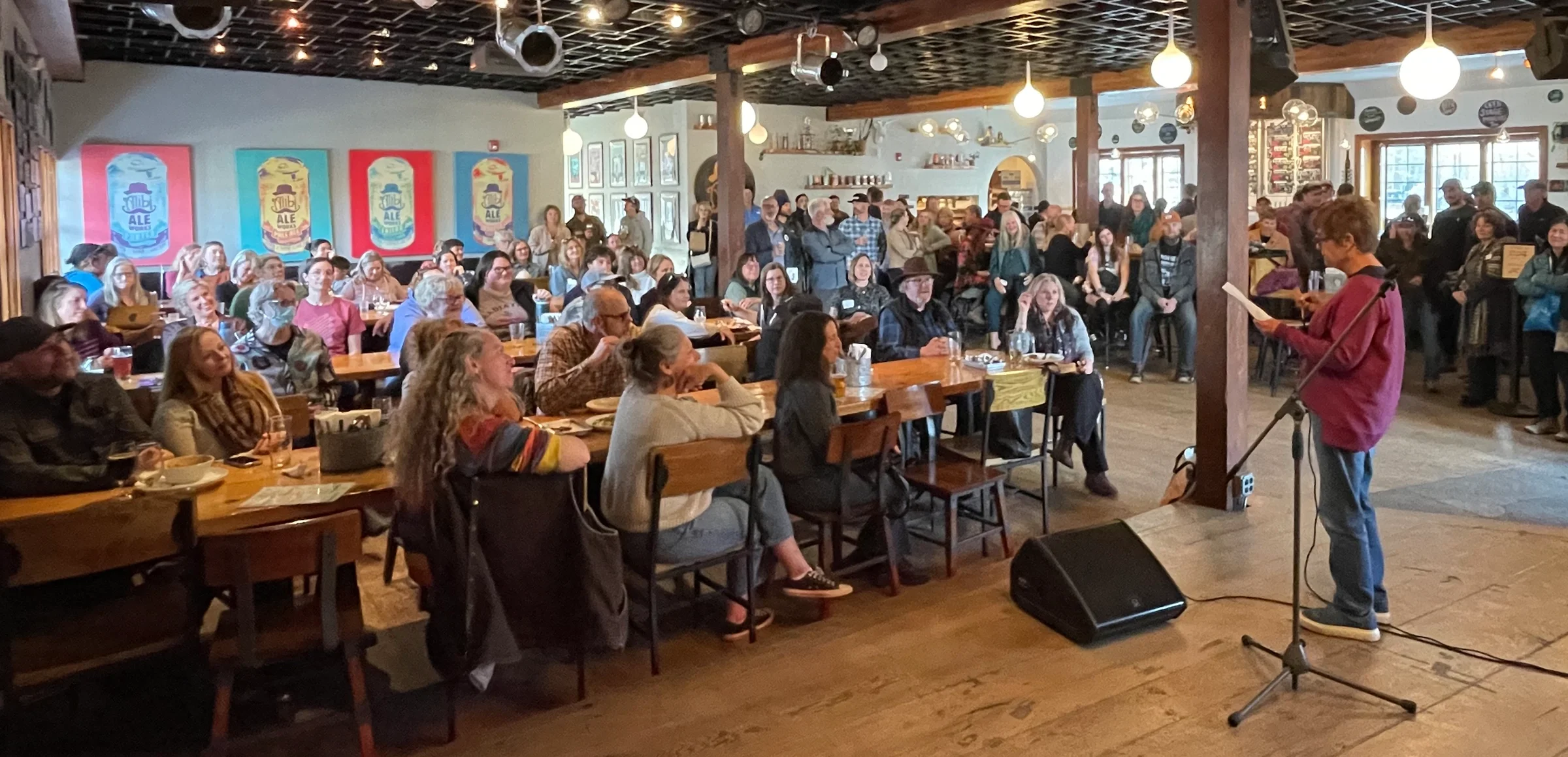 People sitting at tables watching a woman perform poetry at Alibi Ale Works Truckee