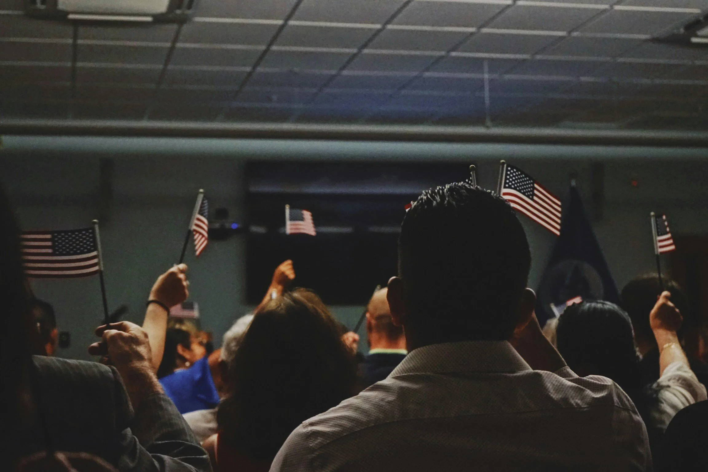 Crowd of people at a rally or event, holding small American flags.