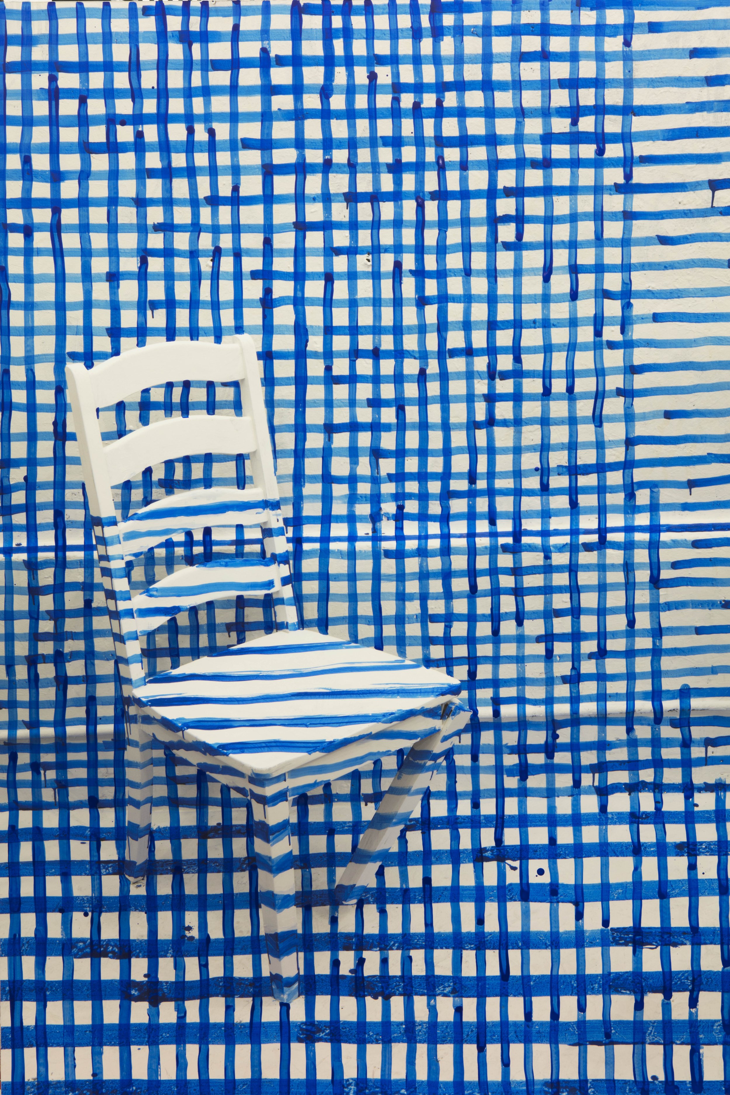 A white chair with blue and white striped fabric in front of a wall and floor decorated with a blue and white checkered pattern.