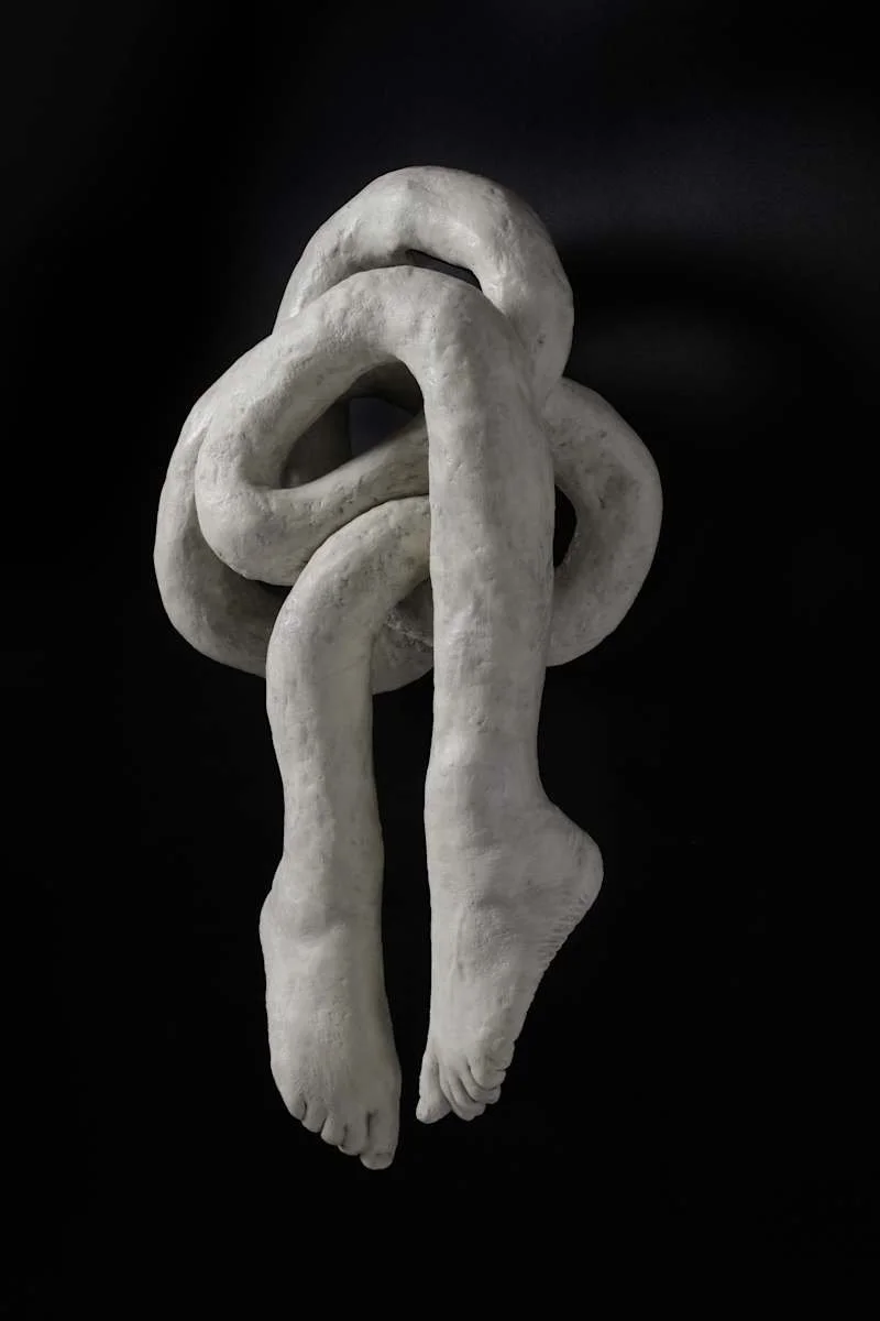 A sculpture of two intertwined hands made of light-colored material on a black background.