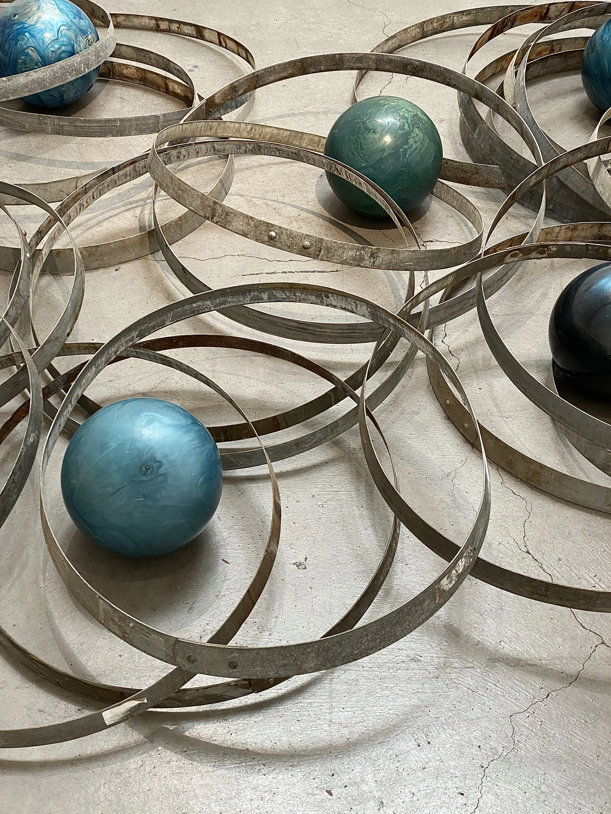 Decorative metal rings with colorful marbles placed inside and around them on a concrete floor.