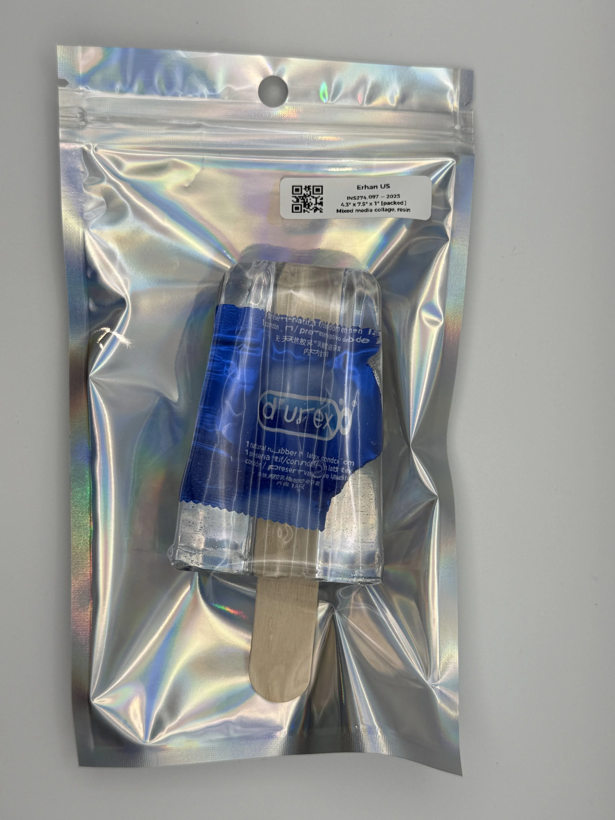 Holographic resealable bag with a labeled sticker and a dildo inside, with a wooden stick at the bottom.