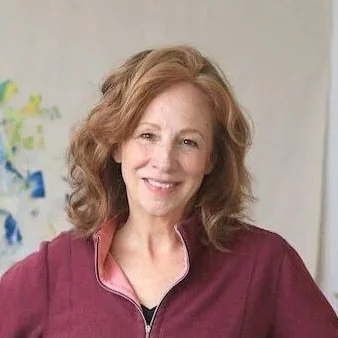 Portrait of a smiling woman with shoulder-length red hair, wearing a maroon jacket.