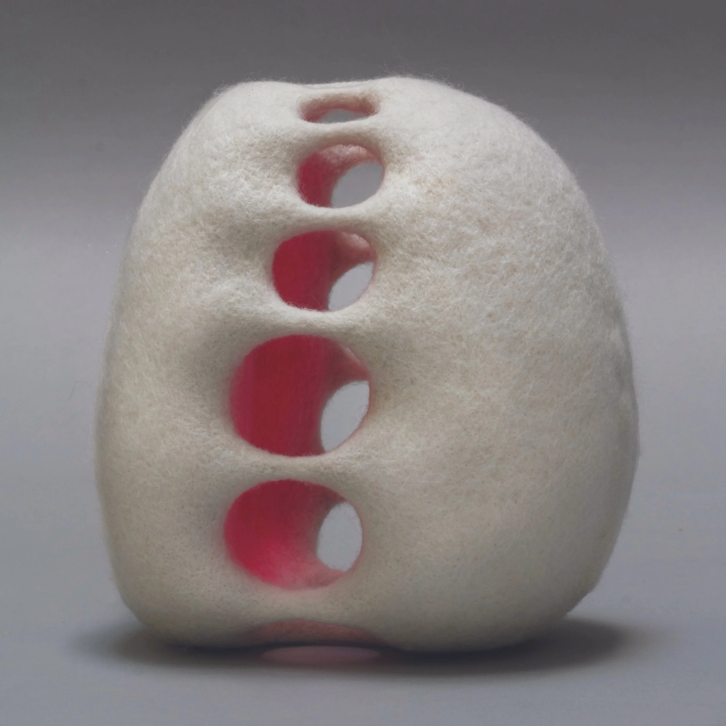 A white foam sponge with multiple circular holes, placed against a grey background.