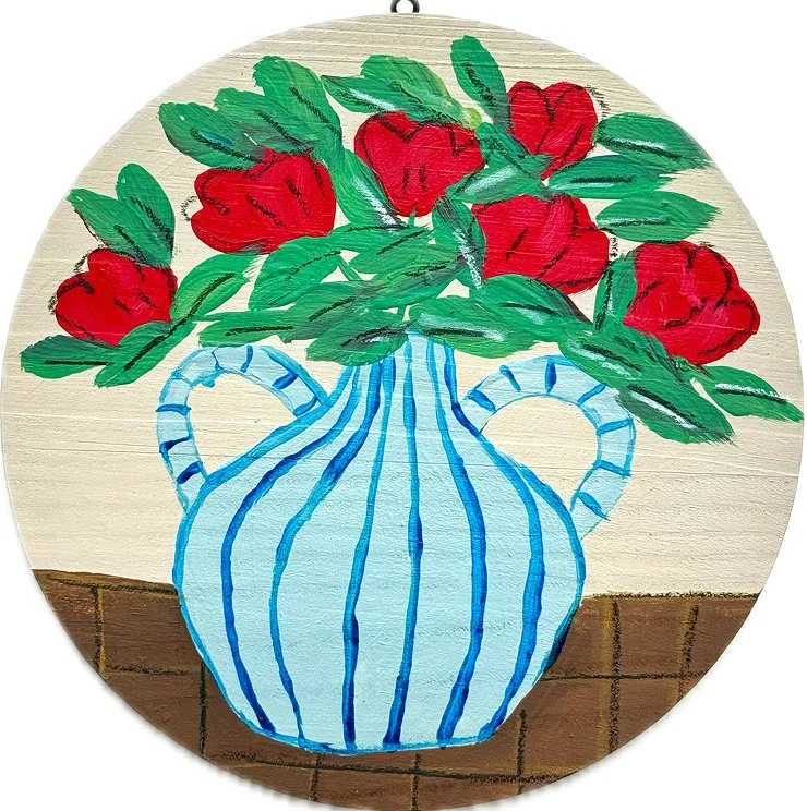 Drawing of a blue striped vase with red flowers and green leaves on a wooden surface.
