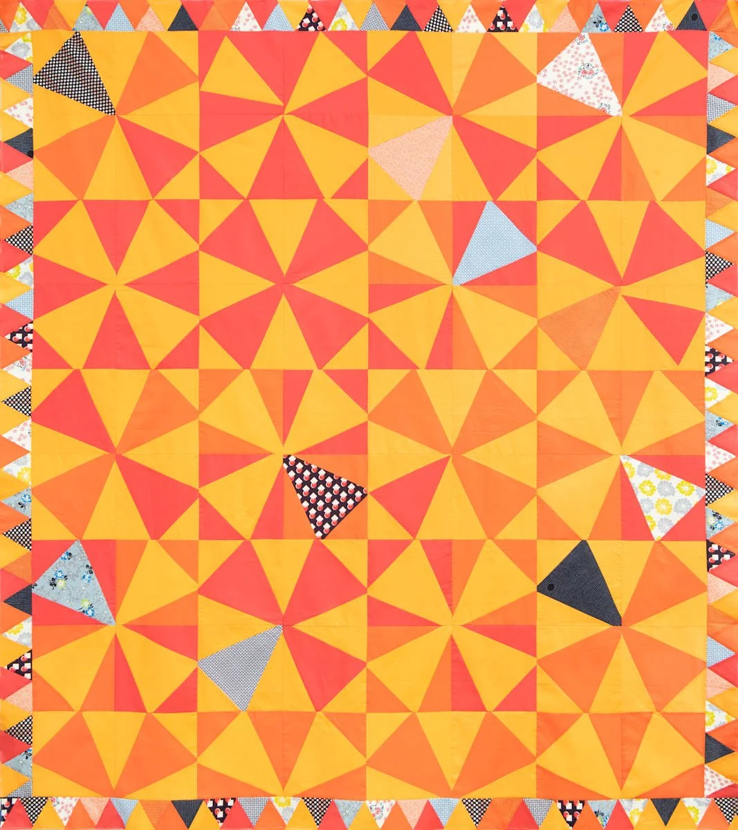 A colorful quilt with a pattern of orange, yellow, and red triangles, and some triangular patches with various patterns and colors around the border.