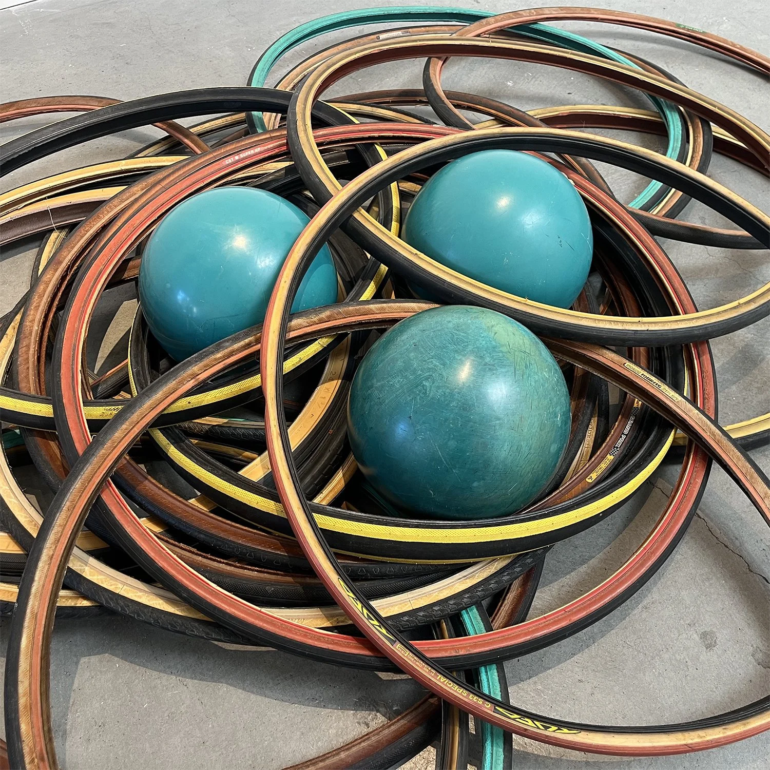 Three blue balls amidst numerous tangled rubber hoses on a concrete floor.