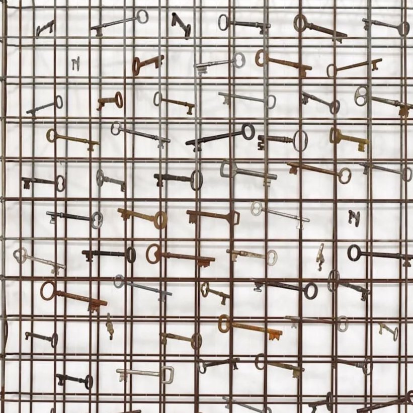 A wall with a grid of metal bars holding various antique keys in different sizes and colors.