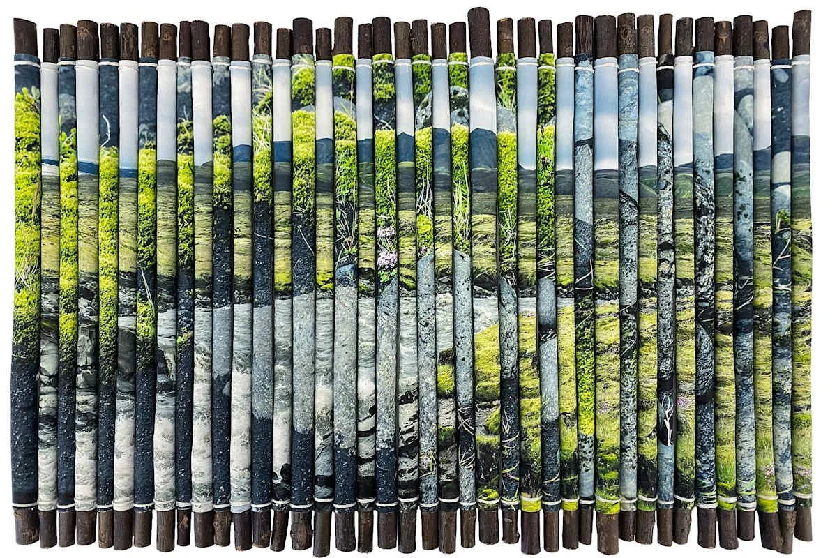 Beach scene with rocks, greenery, and blue sky on wooden sticks.