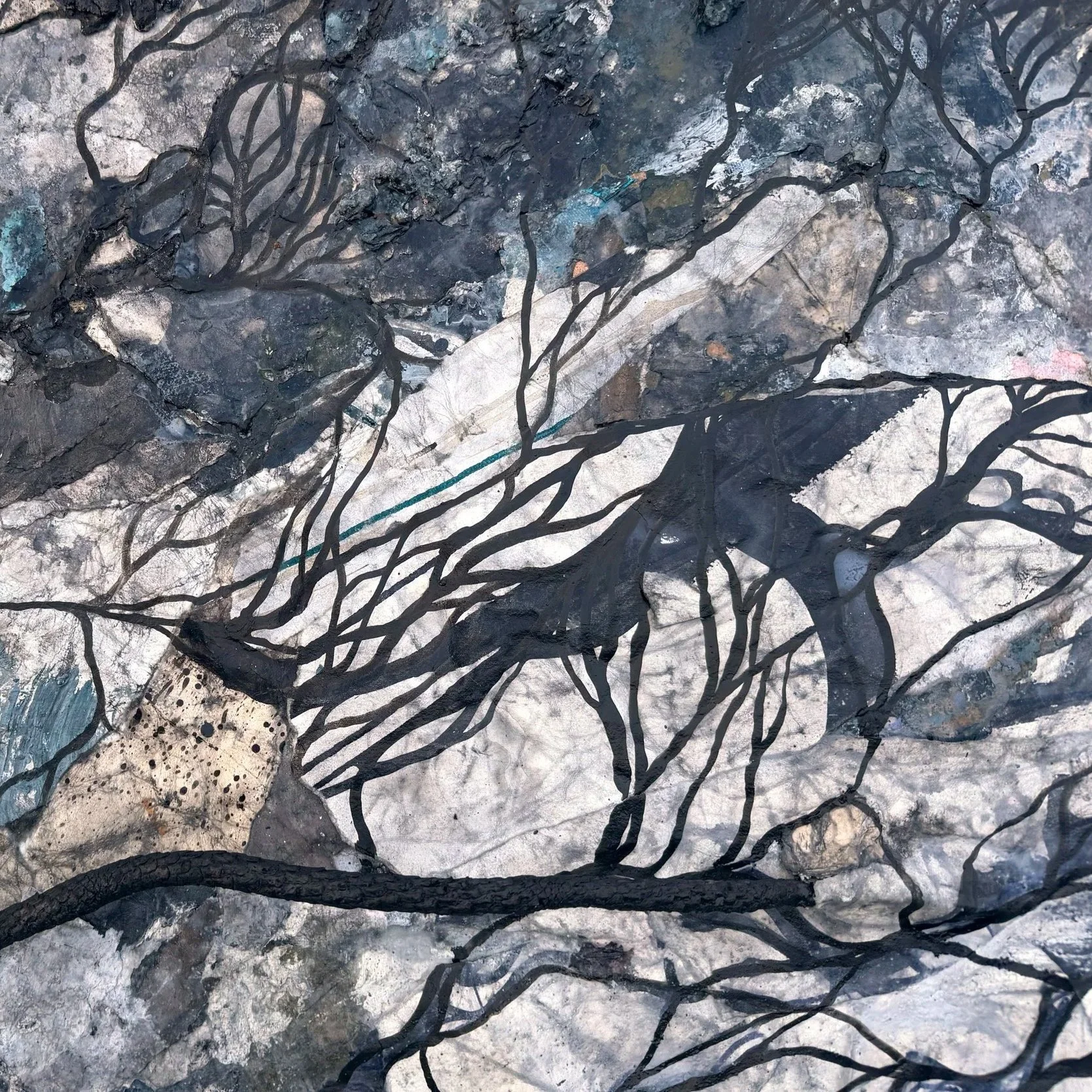 An abstract artwork depicting black, twisted tree branches over a background of rocks, paper, and textured materials in shades of gray, white, black, and hints of blue.