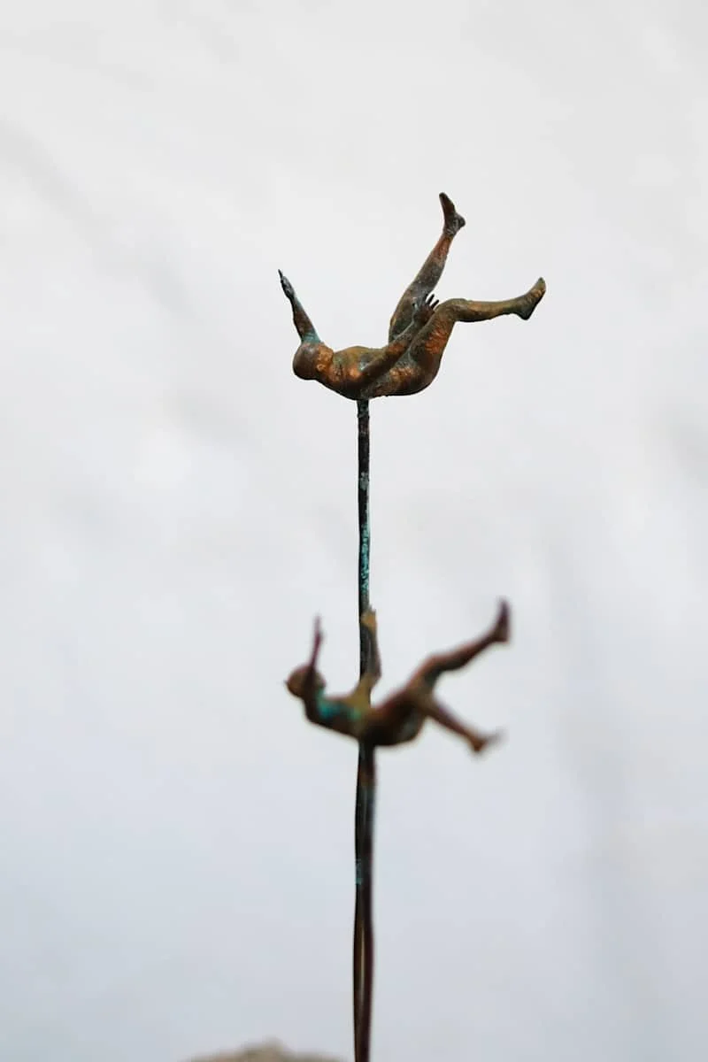 A metal sculpture of two upside-down human figures on top of each other, set against a gray sky