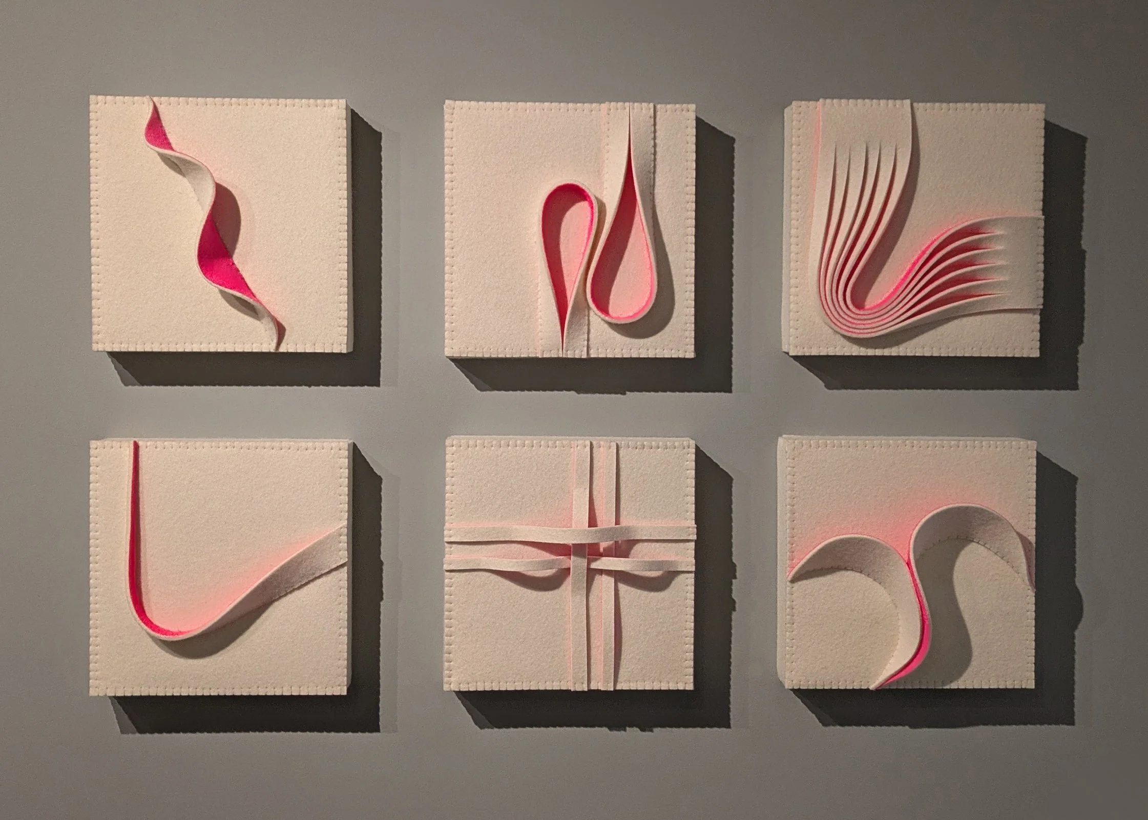 Six white square art pieces arranged in two rows of three, each with pink paper strips folded and shaped into different designs.