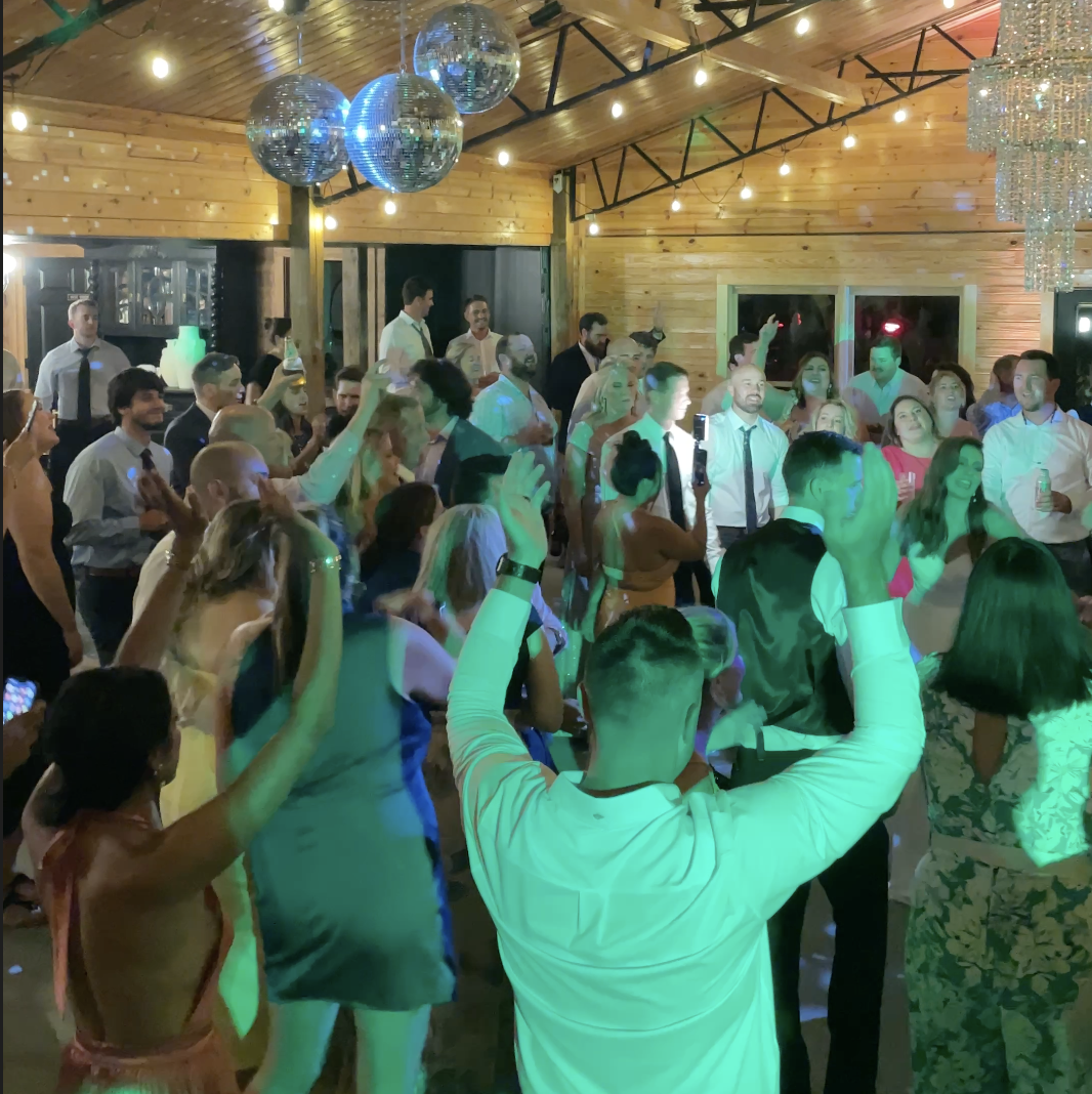 Guests dancing at a lively party with disco balls and colorful lighting in a wooden venue.