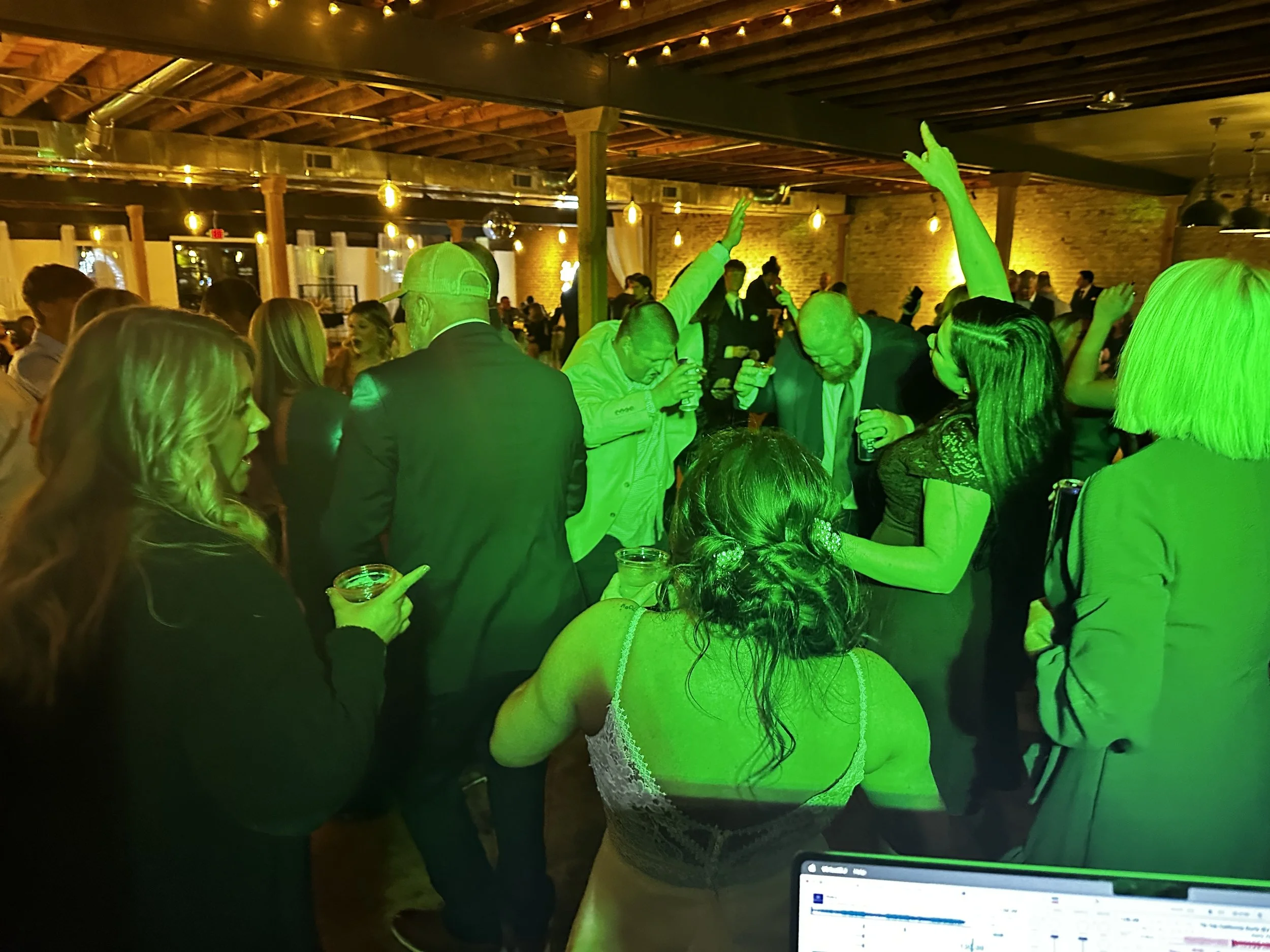 People dancing and socializing at a party venue illuminated by warm lights, with some holding drinks and one person taking a photo.