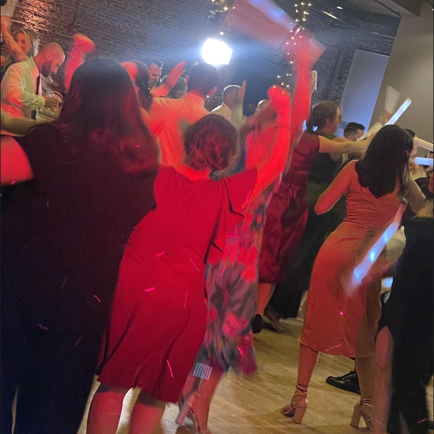 People dancing at a party with colorful lighting in a dimly lit room decorated with string lights.