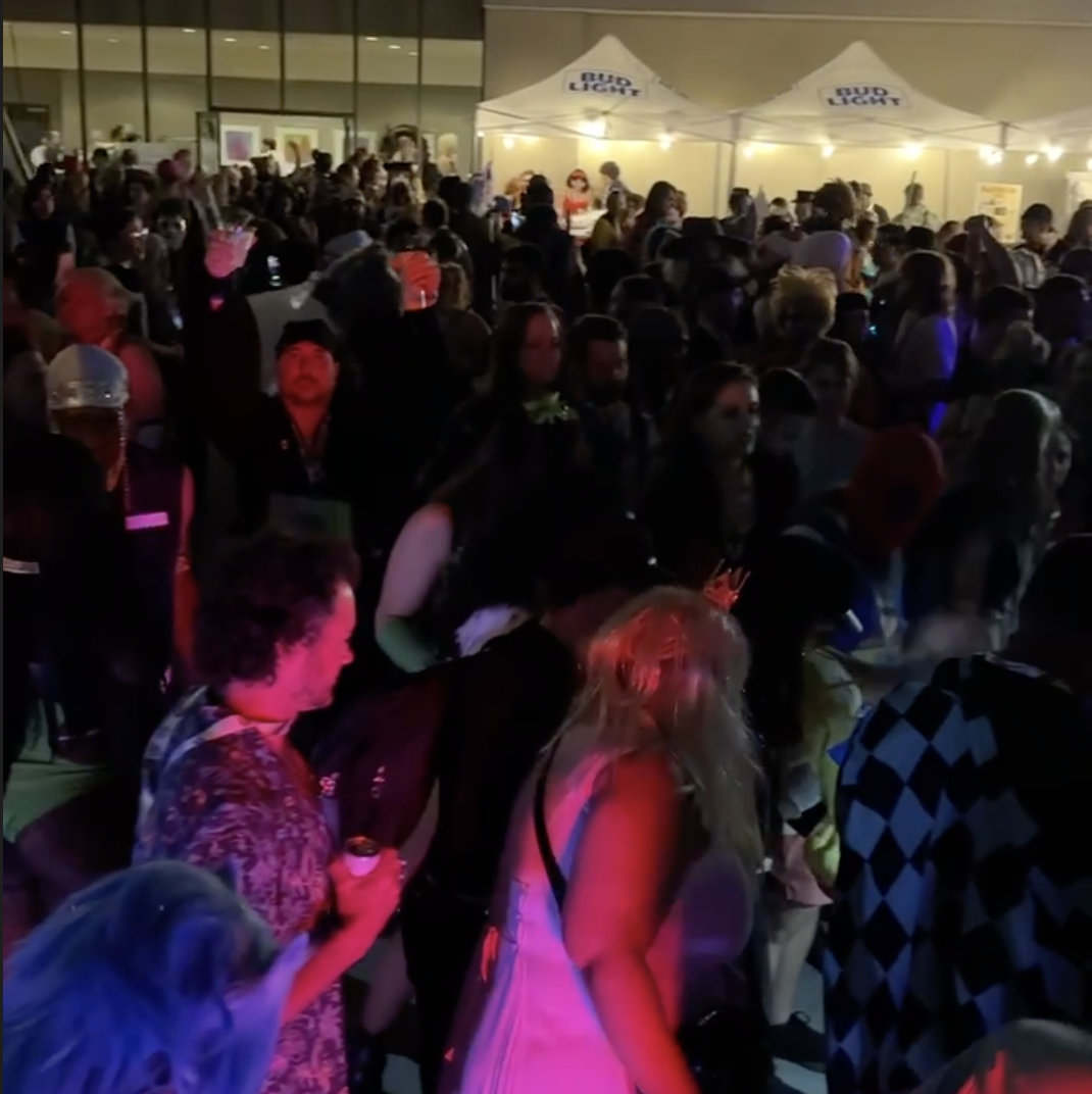 Crowd of people at an outdoor nighttime dance party at DragonCon in Atlanta with tents and string lights, some dancing and socializing.