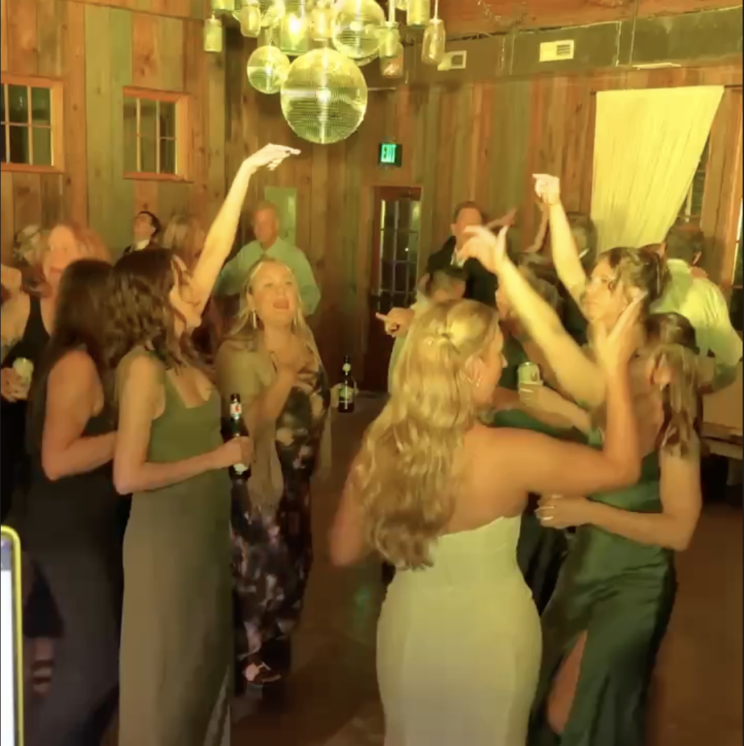 Women dancing and celebrating at a wedding with disco balls hanging from the ceiling.