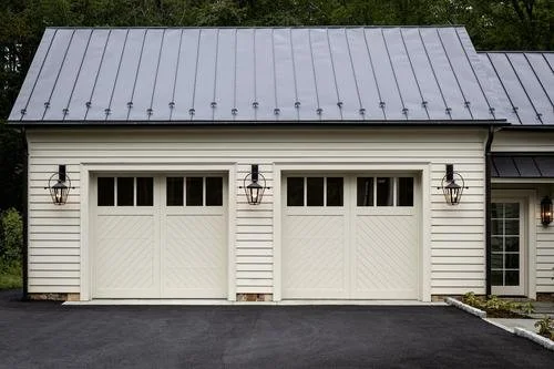 White garage doors with black lantern-style lights on a white building with gray metal roof.