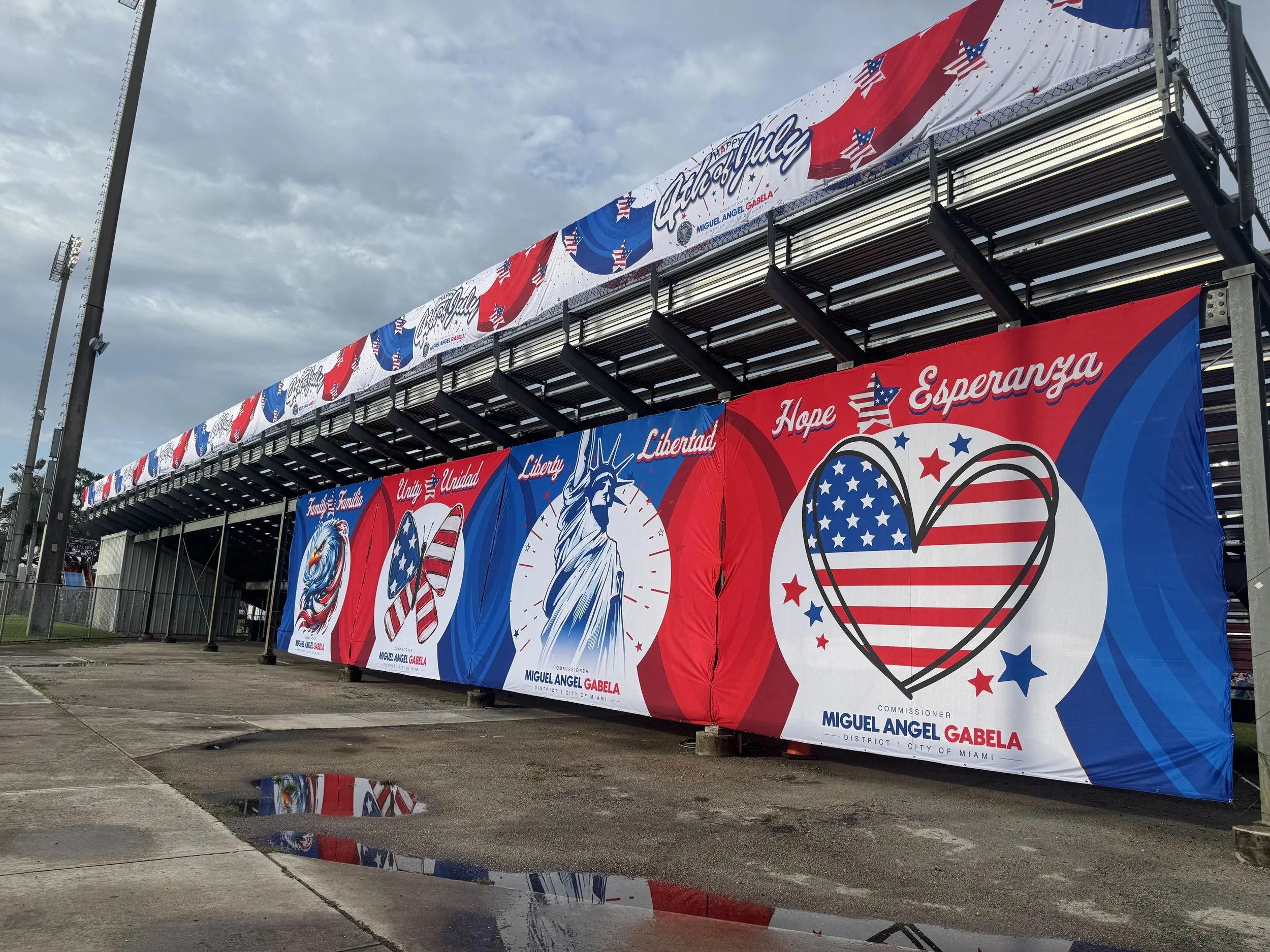 Large patriotic banners with American flags, the Statue of Liberty, and hearts featuring the American flag, supporting Miguel Angel Gabela's campaign for Miami District 1.