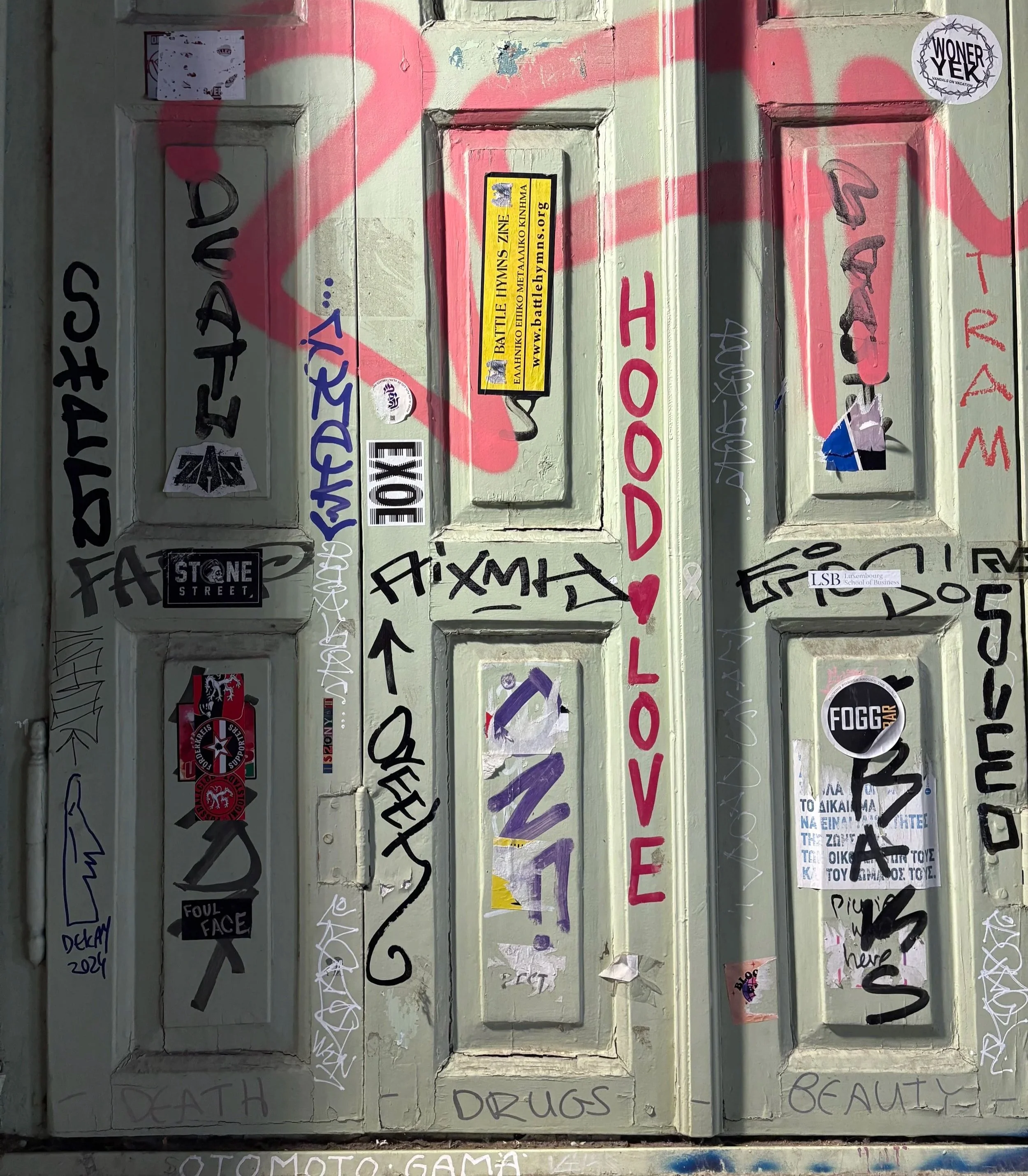 An exterior door covered with various stickers, graffiti, and handwritten messages. Athens, Greece.