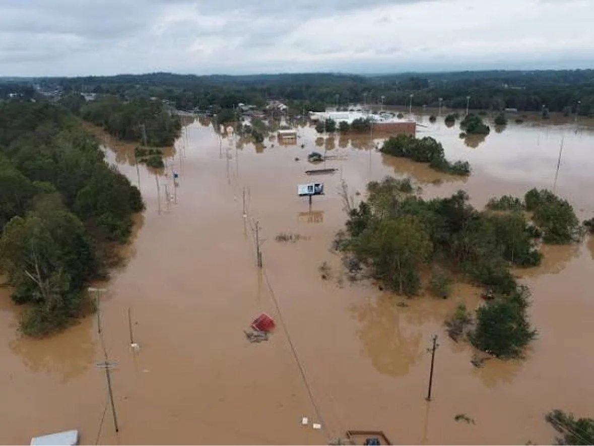 Aerial view of a flooded town with brown floodwater surrounding trees and buildings