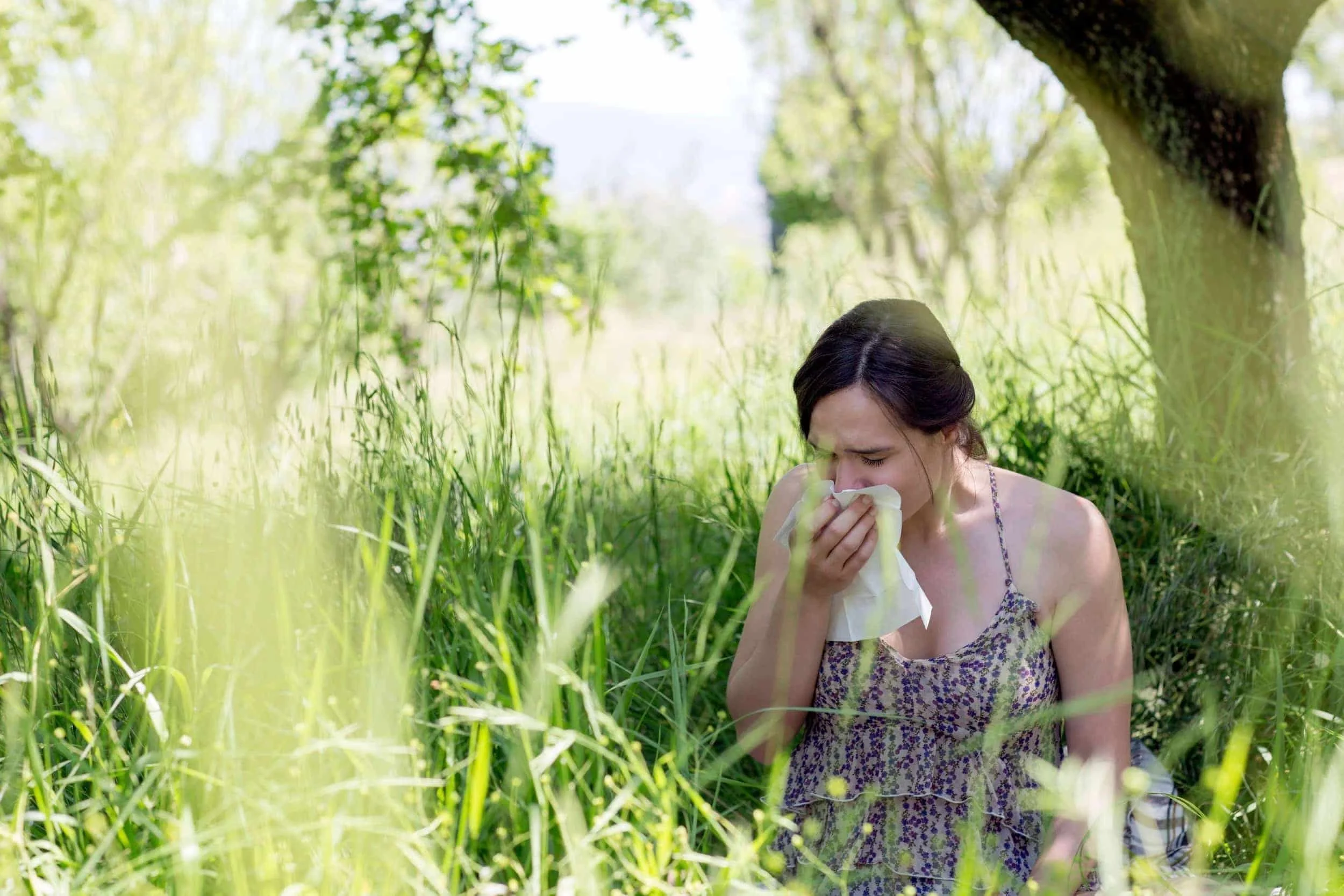 A woman sitting in tall grass experiencing environmental allergies.