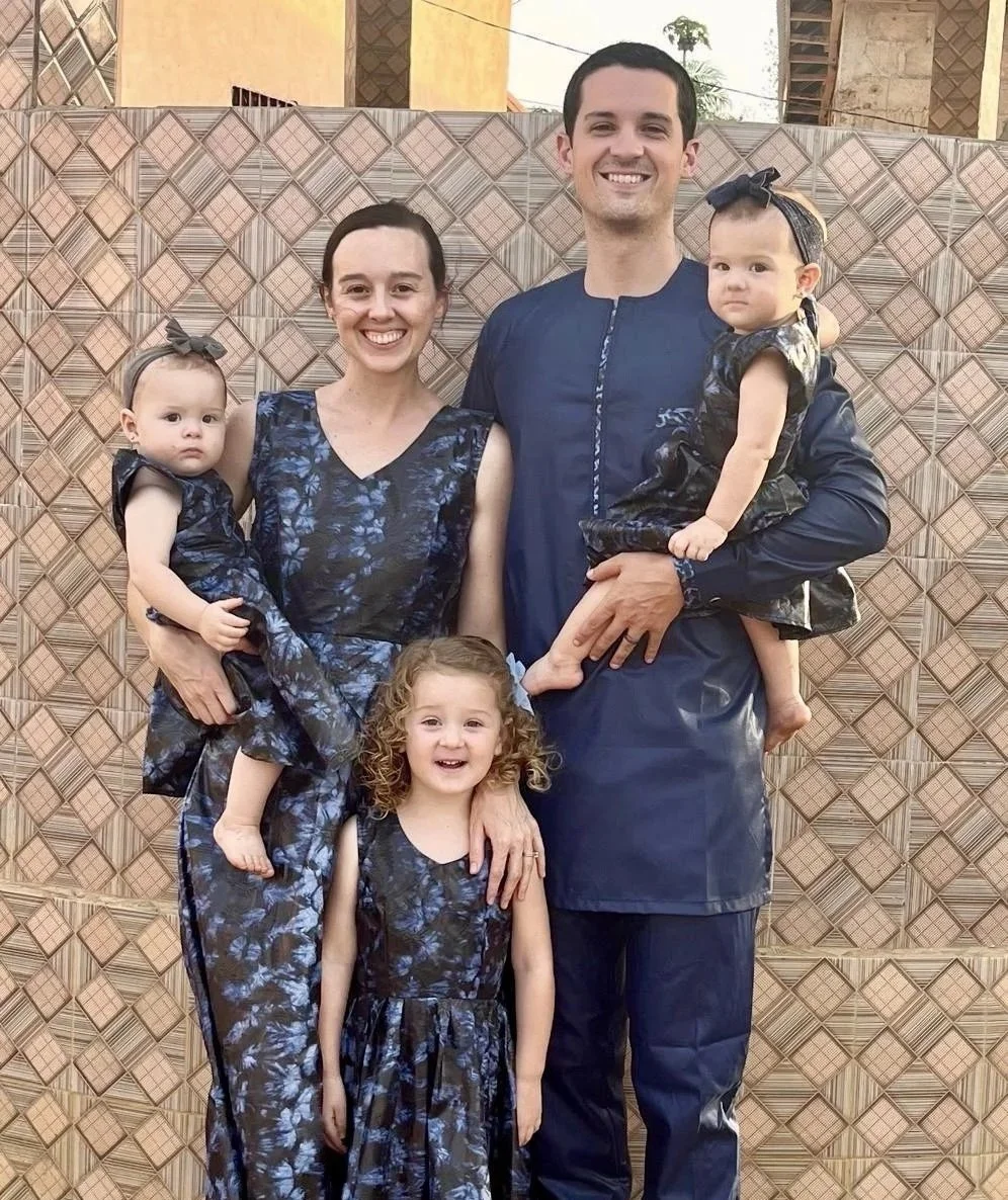 A family of five posing outdoors in front of a patterned fence, dressed in matching blue and black floral outfits.