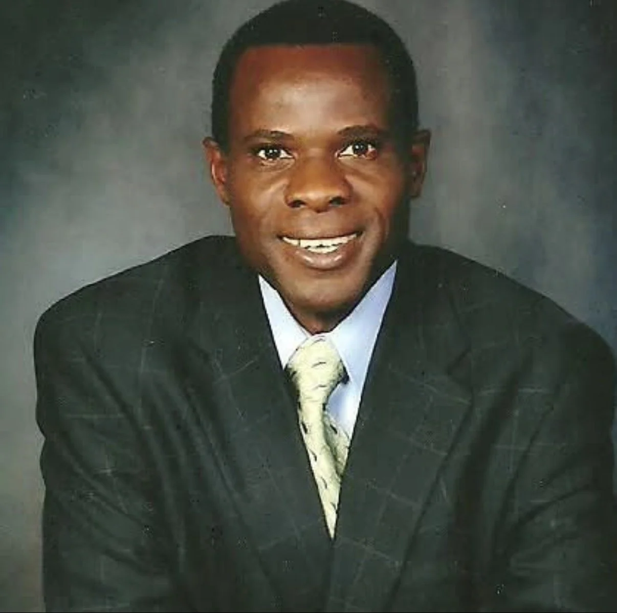 A smiling man in a suit and tie posing for a professional portrait against a dark background.