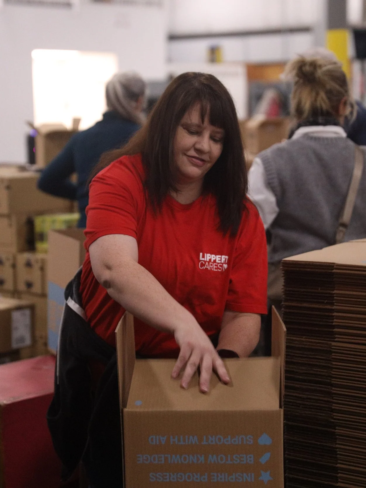 Woman in red shirt packing boxes in a warehouse.