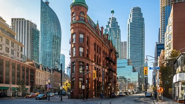 A historic red brick building at a busy city intersection surrounded by modern skyscrapers and traffic signals.