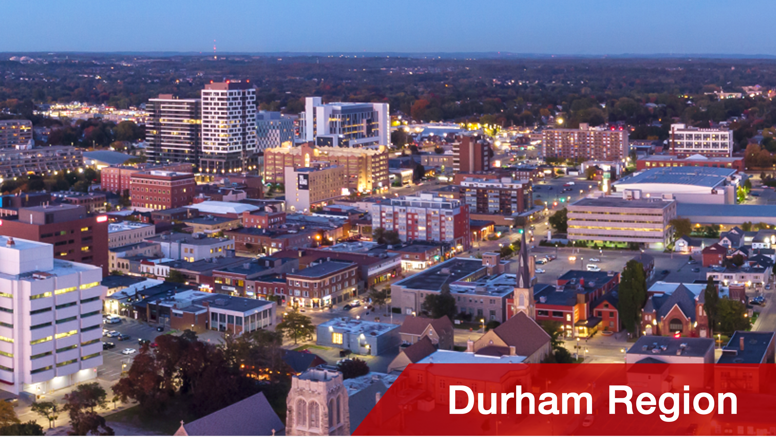 Aerial view of Durham Region cityscape at dusk with illuminated buildings, streets, and a church in the foreground, and the text 'Durham Region' in a red banner at the bottom.