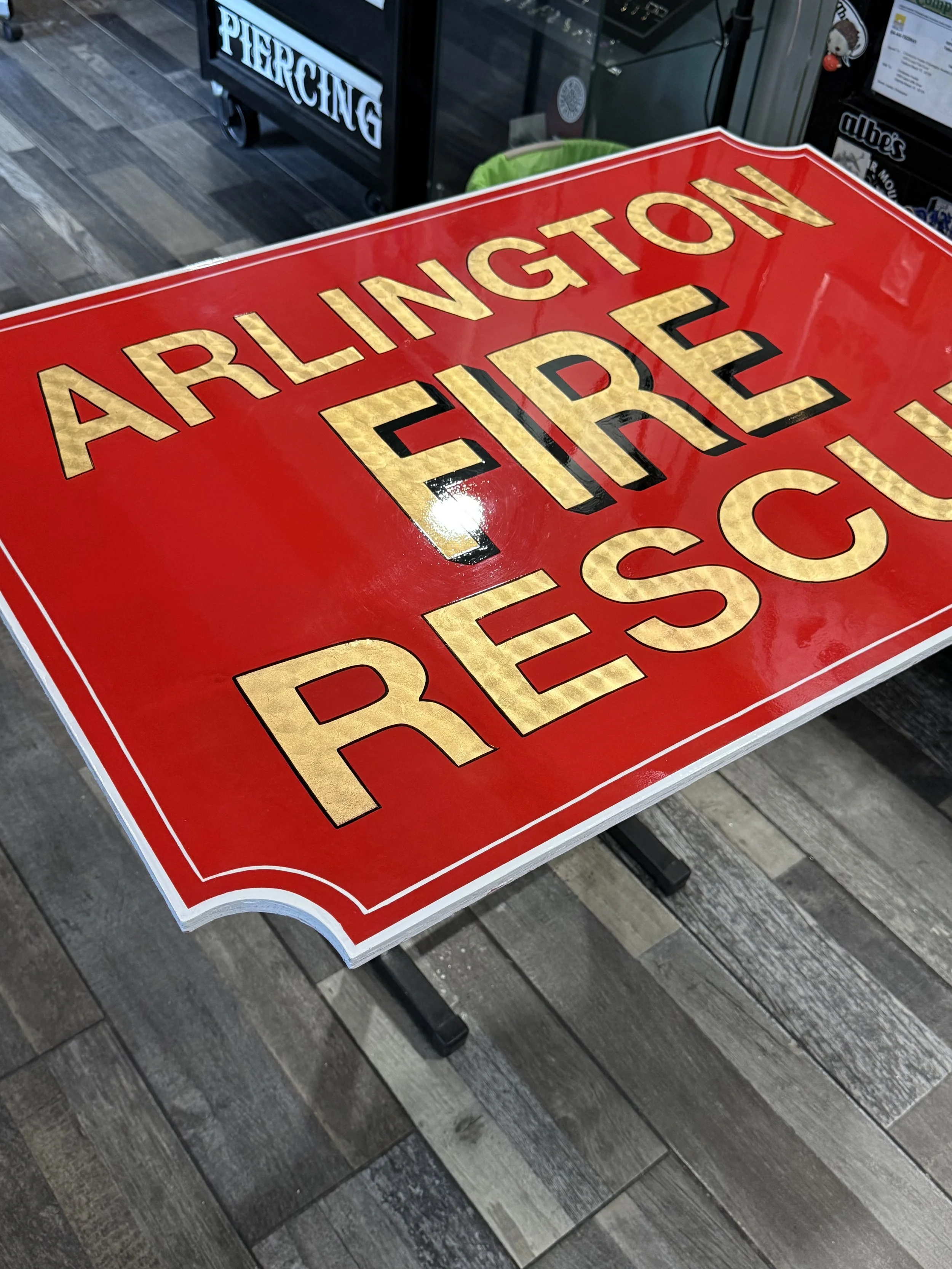 A large red and gold sign that reads 'Arlington Fire Rescue' in gold leaf on a table in an indoor setting.