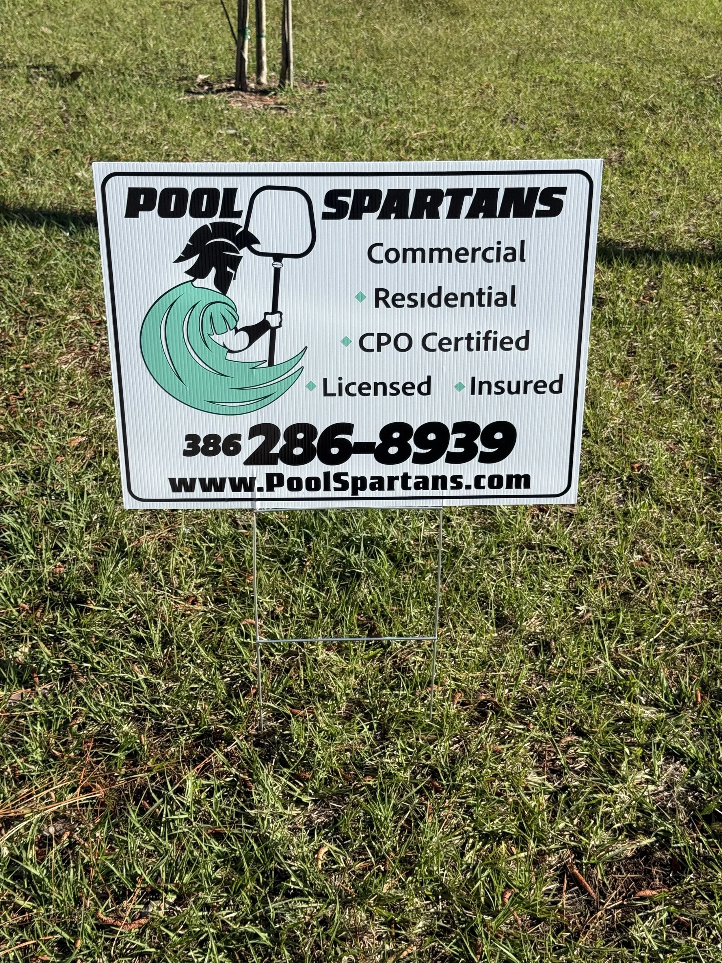Sign for Pool Spartans showing a Spartan warrior holding a net, with contact number and website, on grassy ground.