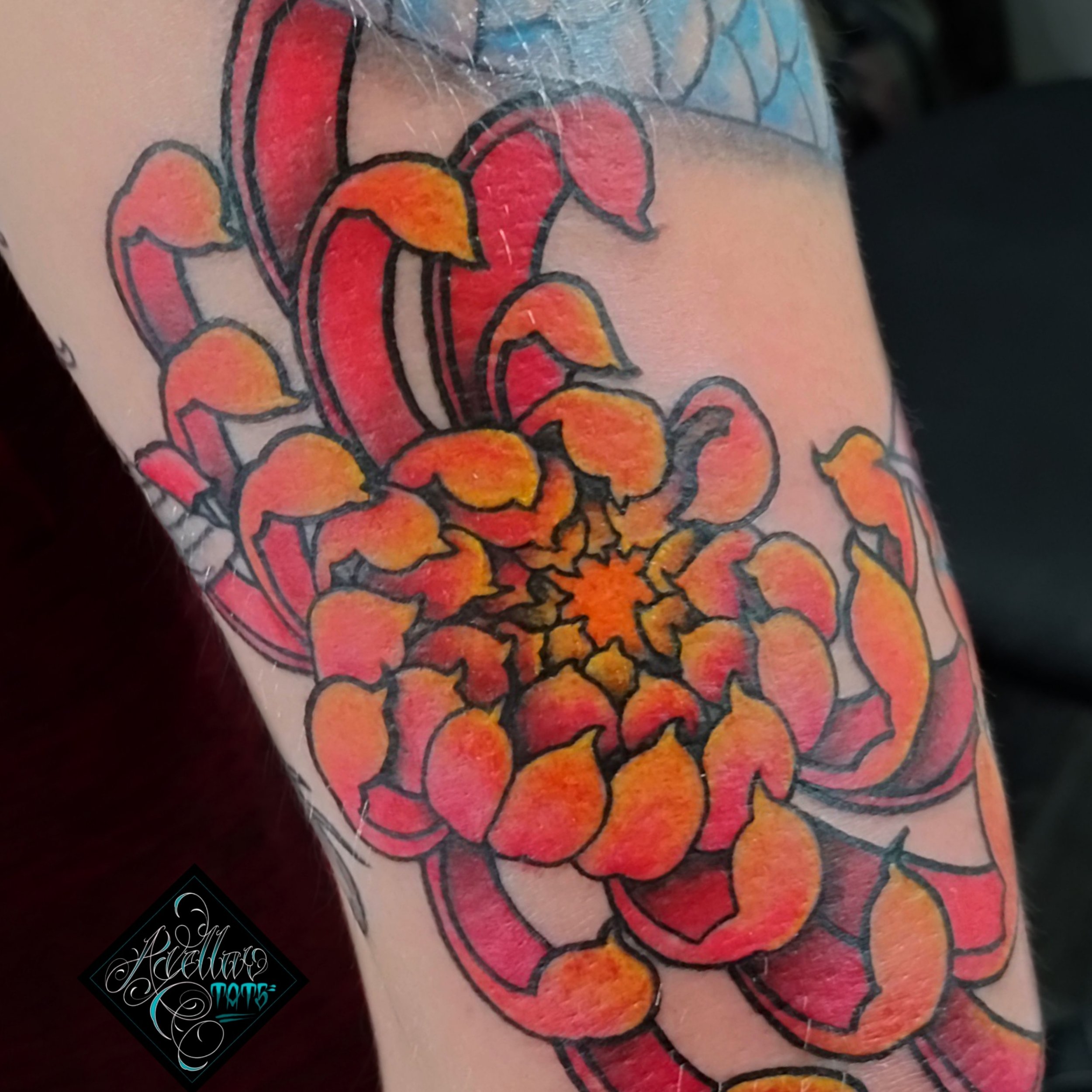 Close-up of a colorful tattoo of a blooming flower with orange and pink petals on a person's arm.